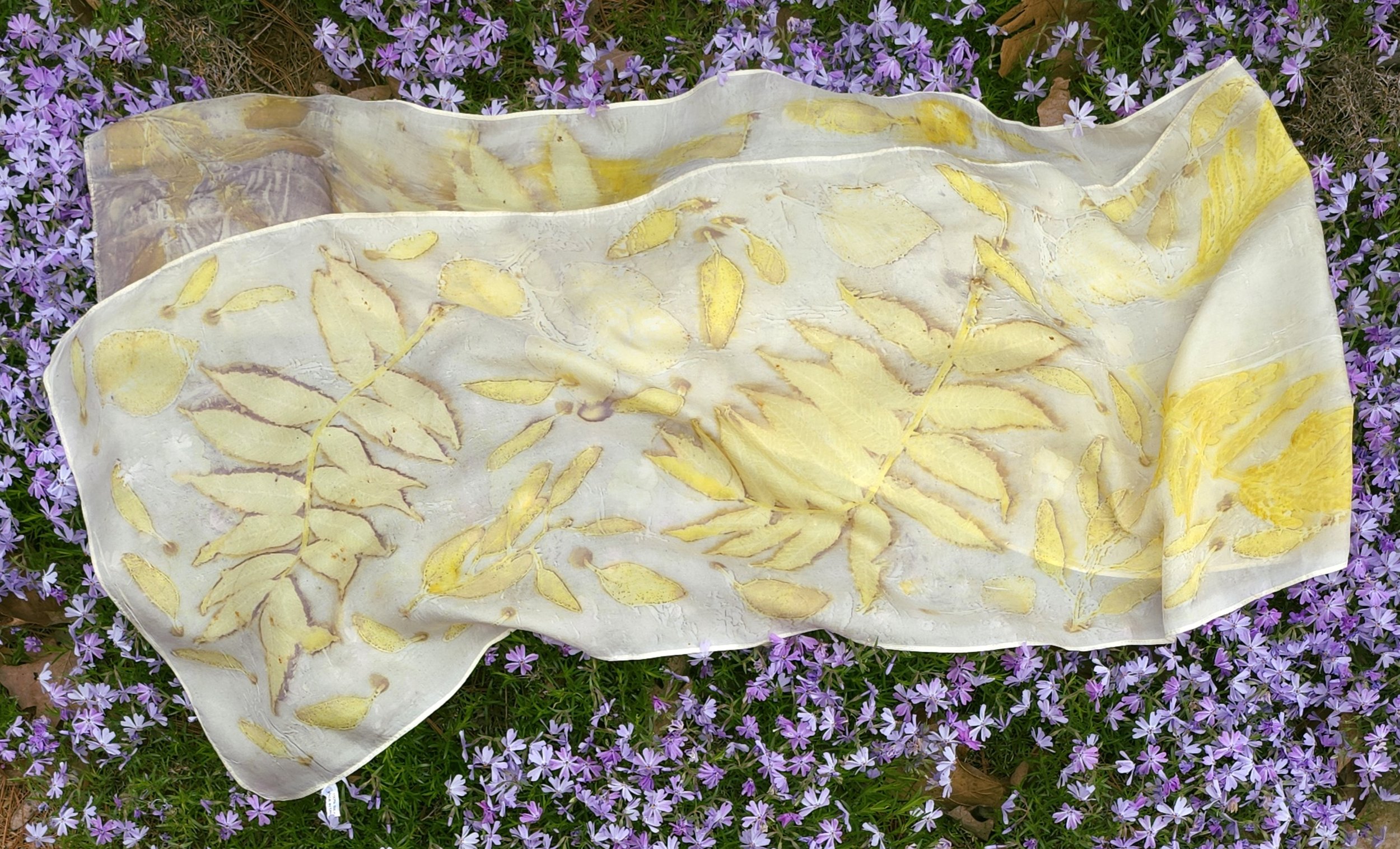 Naturally dyed eco-printed silk scarf using wildcrafted Sumac leaves, wildcrafted Mimosa leaves, eucalyptus, and hydrangea flowers with a ferrous sulfate "iron blanket" method, modified with soda ash. 72x14”. 2024