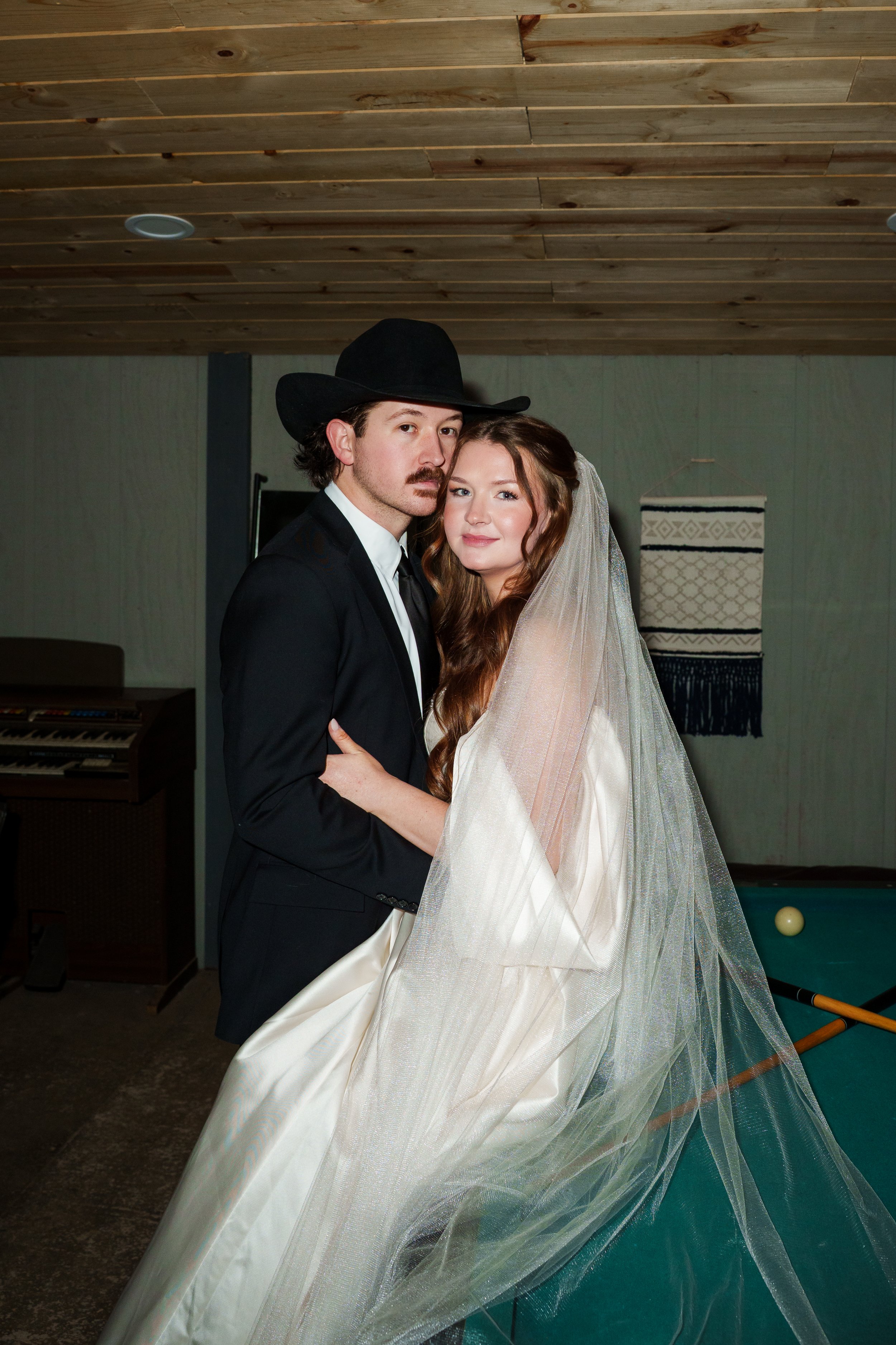Bride sitting on the pool table in the groom's suite with the groom standing in front of her