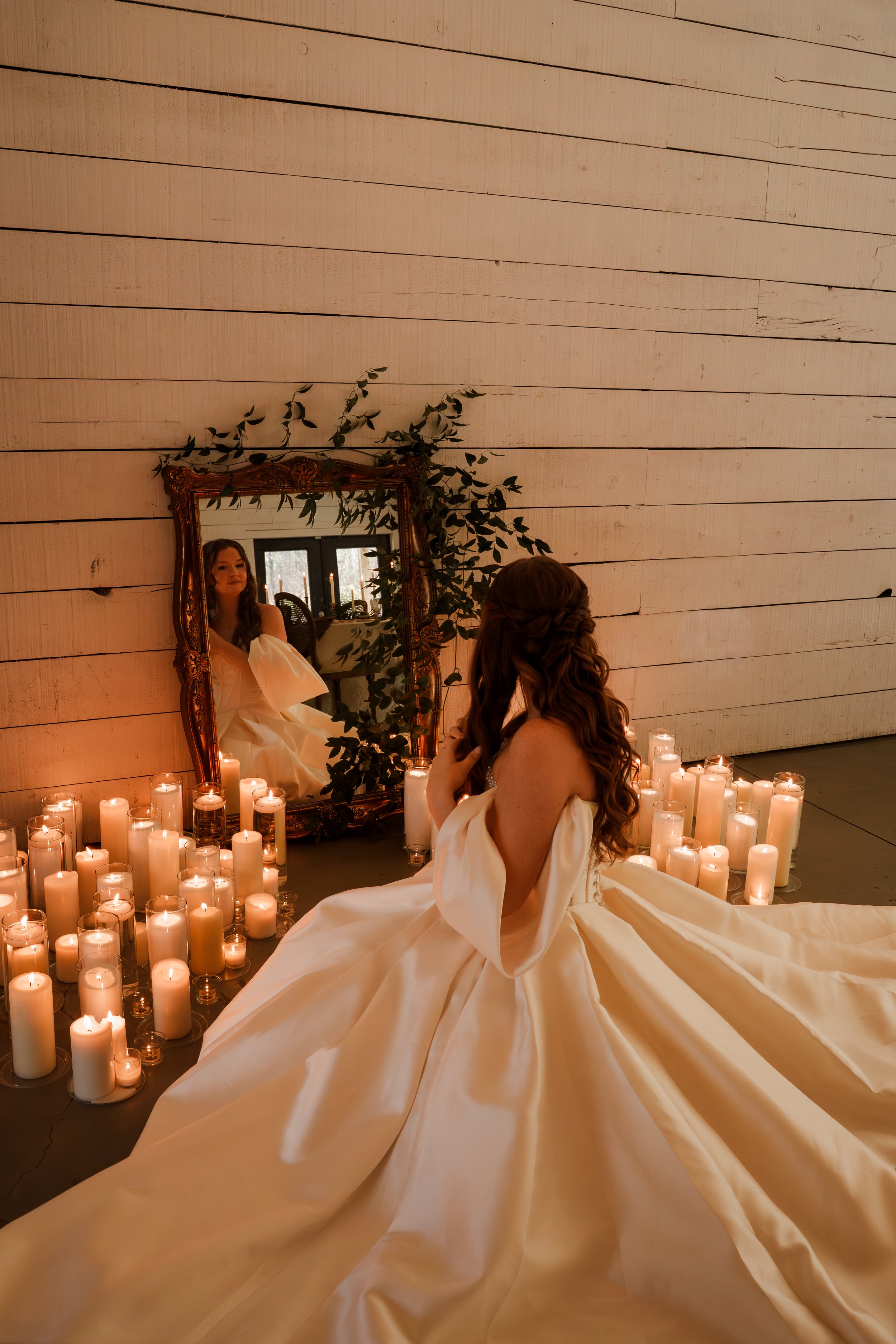 Bride fixing her hair in the mirror surrounded by candles