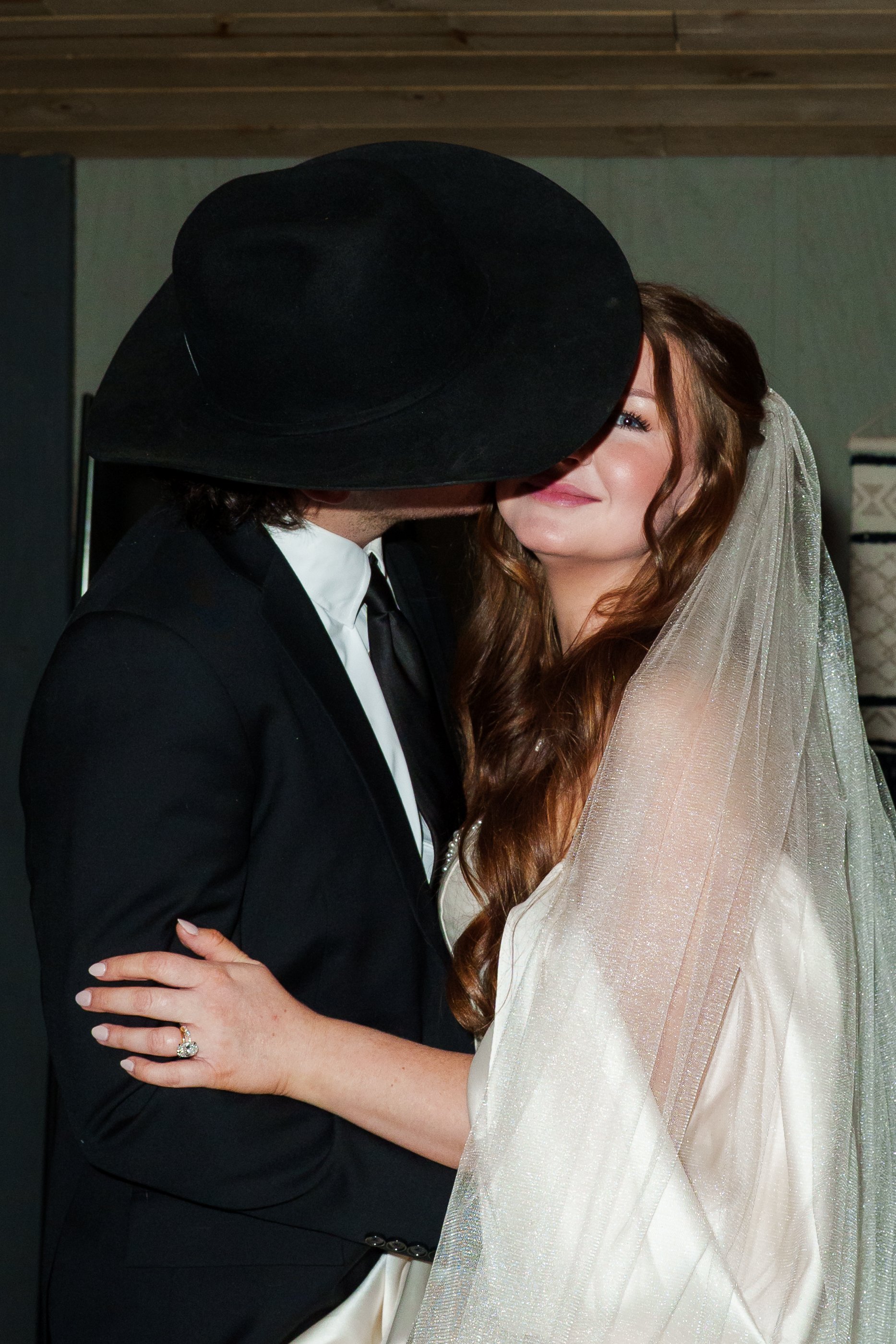 Groom kissing the Bride's cheek while wearing a cowboy hat