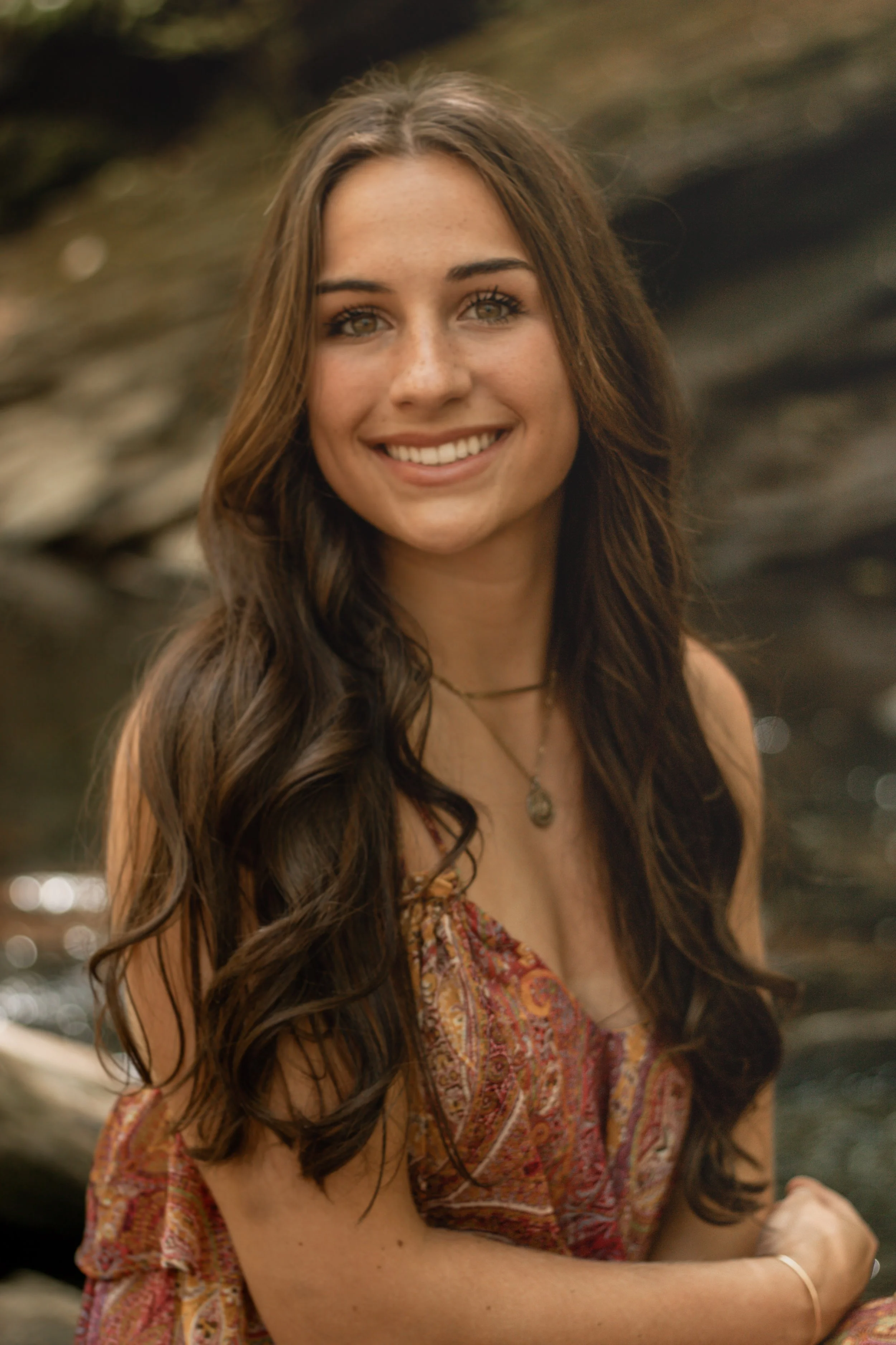 Senior portraits by a creek/river. Girl in a long colorful dress by a creek/river.