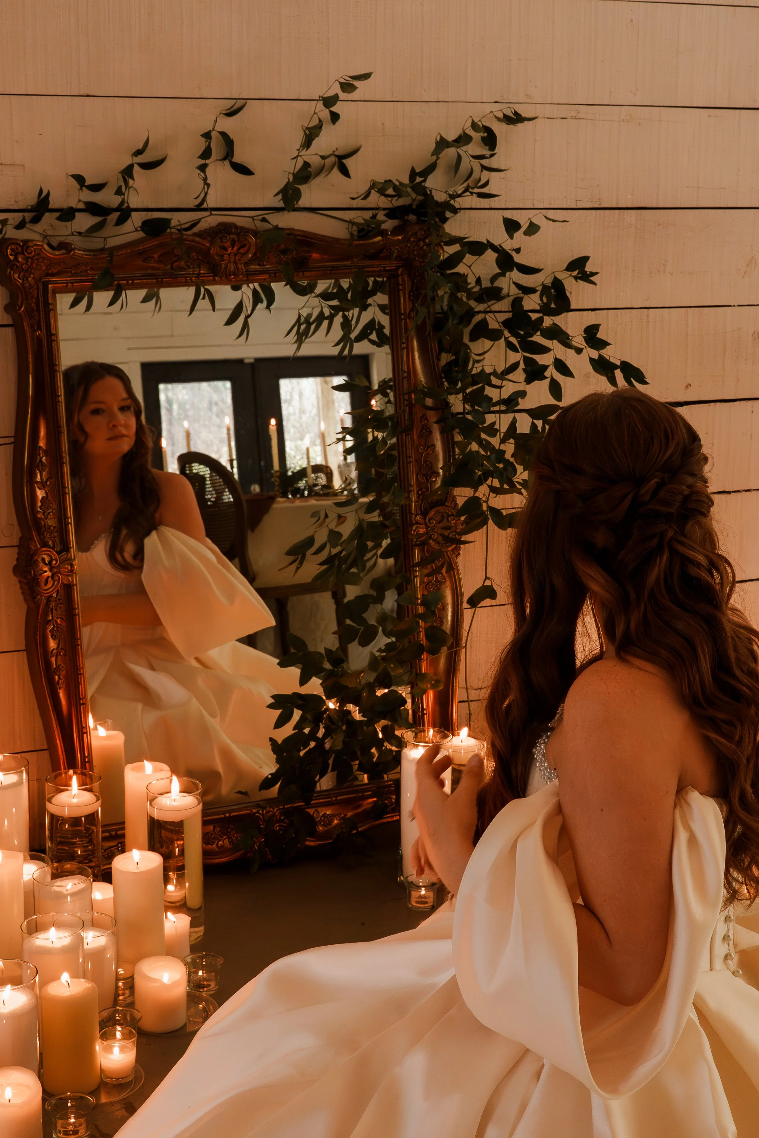 Bride fixing her hair in the mirror surrounded by candles