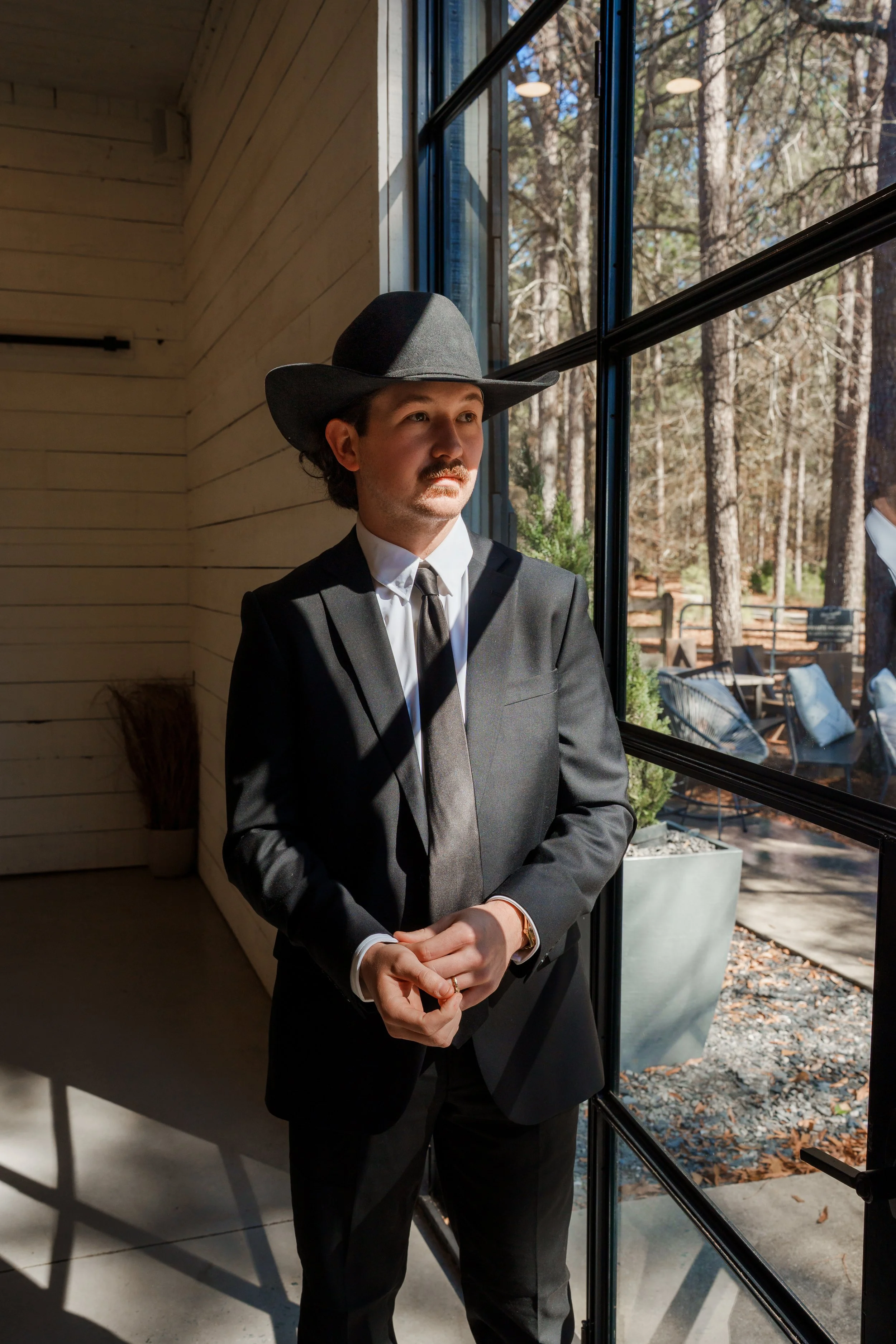 Groom adjusting his suit sleeves while staring out the window