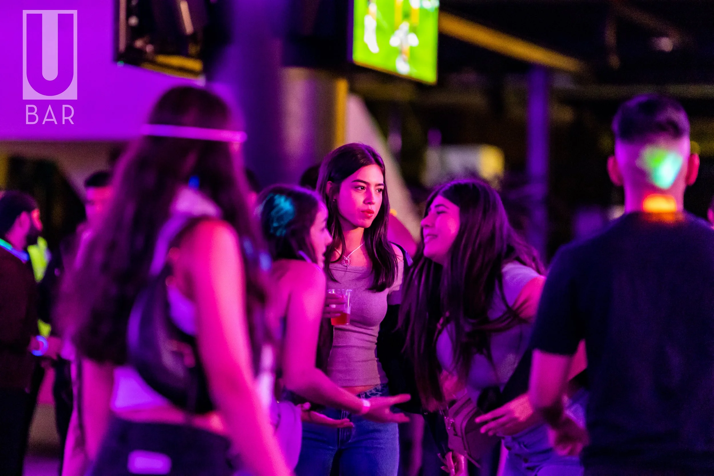 Group of young people socializing at a bar or nightclub with purple and green neon lighting