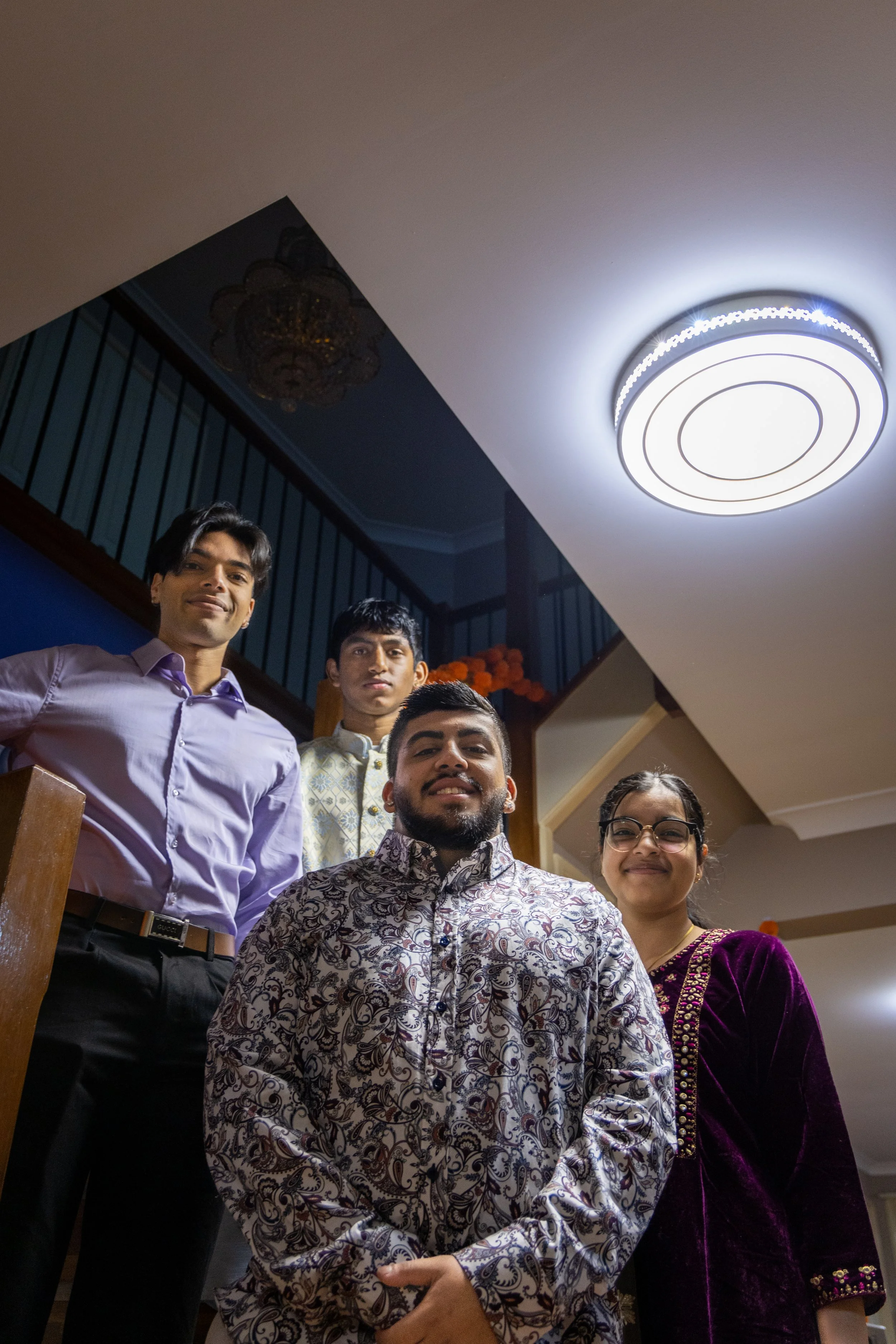 A group of five people posing for a photo indoors, with a ceiling light and staircase in the background.