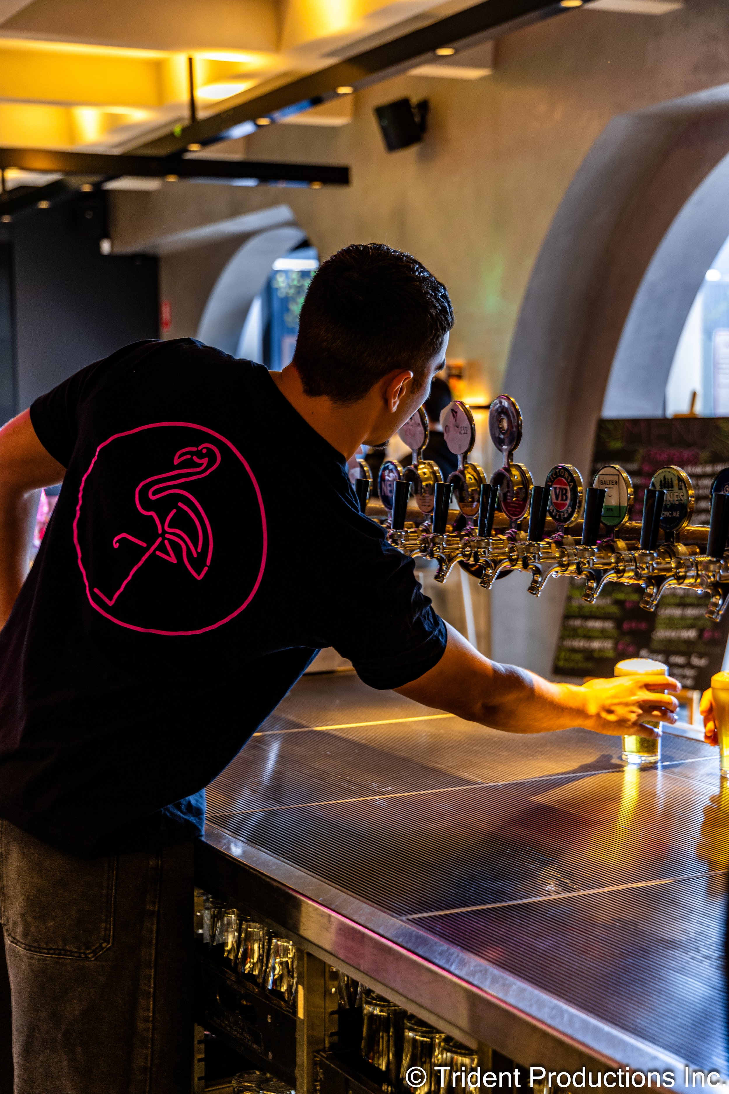 A bartender pours drinks at a bar with multiple beer taps in a modern, dimly lit setting.