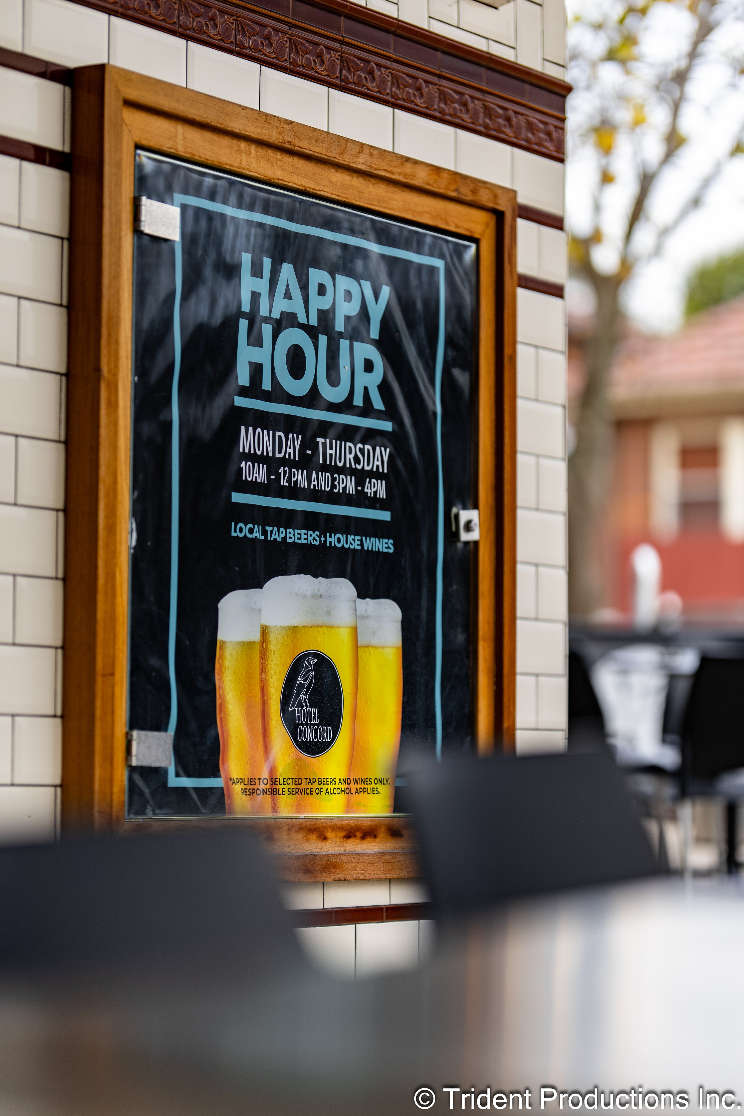 A signboard for Happy Hour at Hotel Concord, offering local tap beers and house wines from Monday to Thursday, 10am to 12pm and 3pm to 4pm, with an image of four glasses of beer.