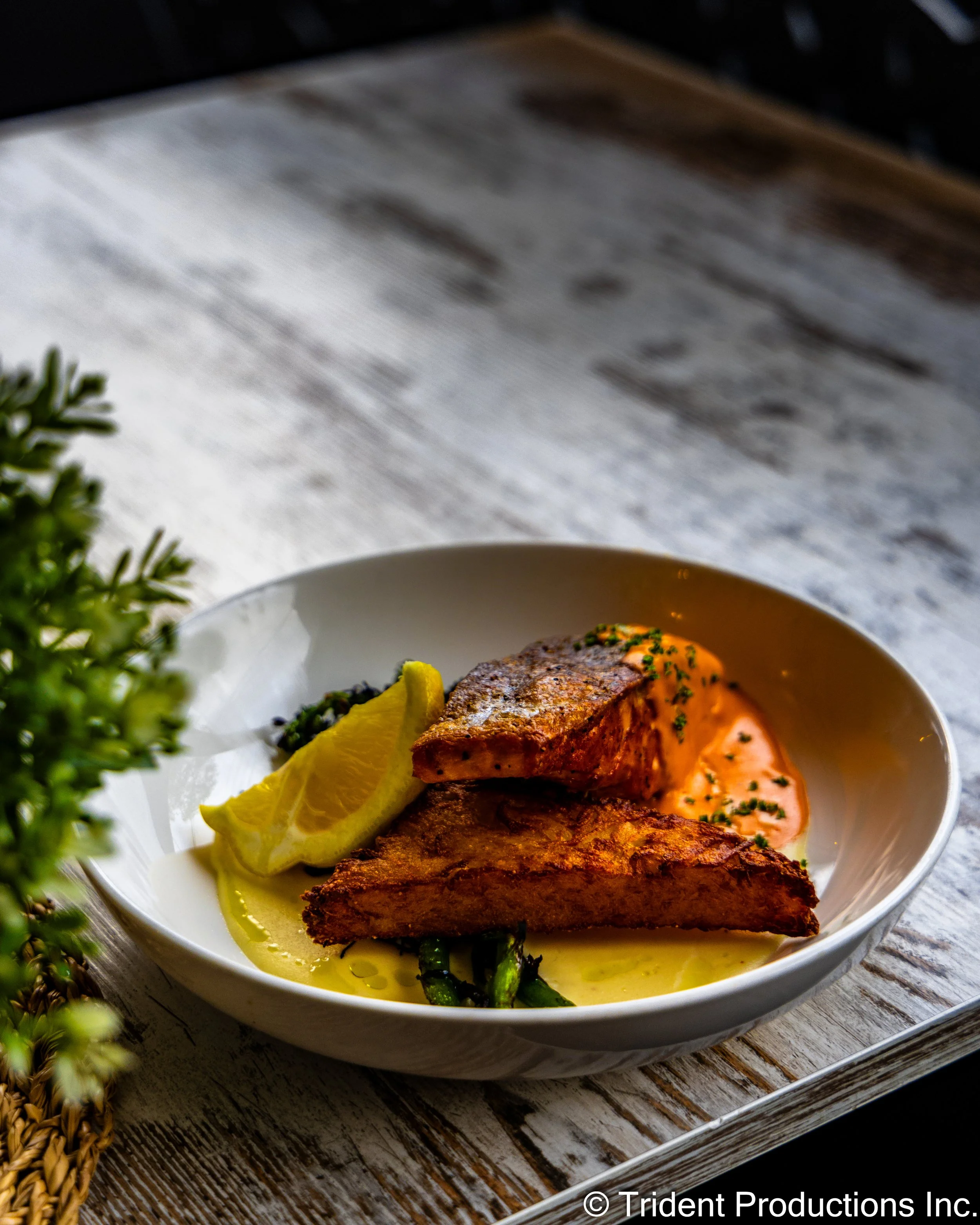 A plate with grilled fish, lemon wedges, green beans, and a creamy orange sauce on a rustic wooden table.