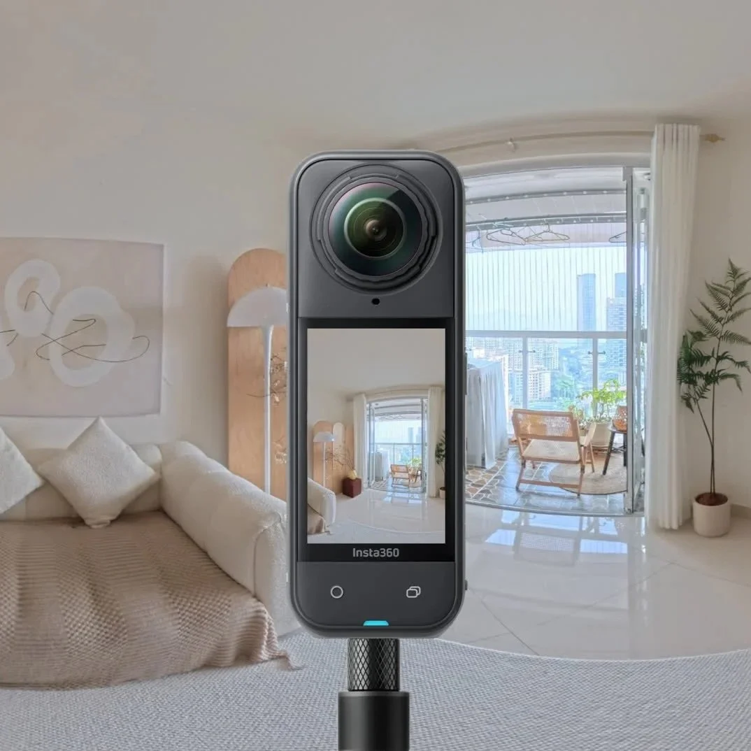 A camera capturing a reflection of a bright, modern living room with large windows, a white sofa, a mirror, and indoor plants.
