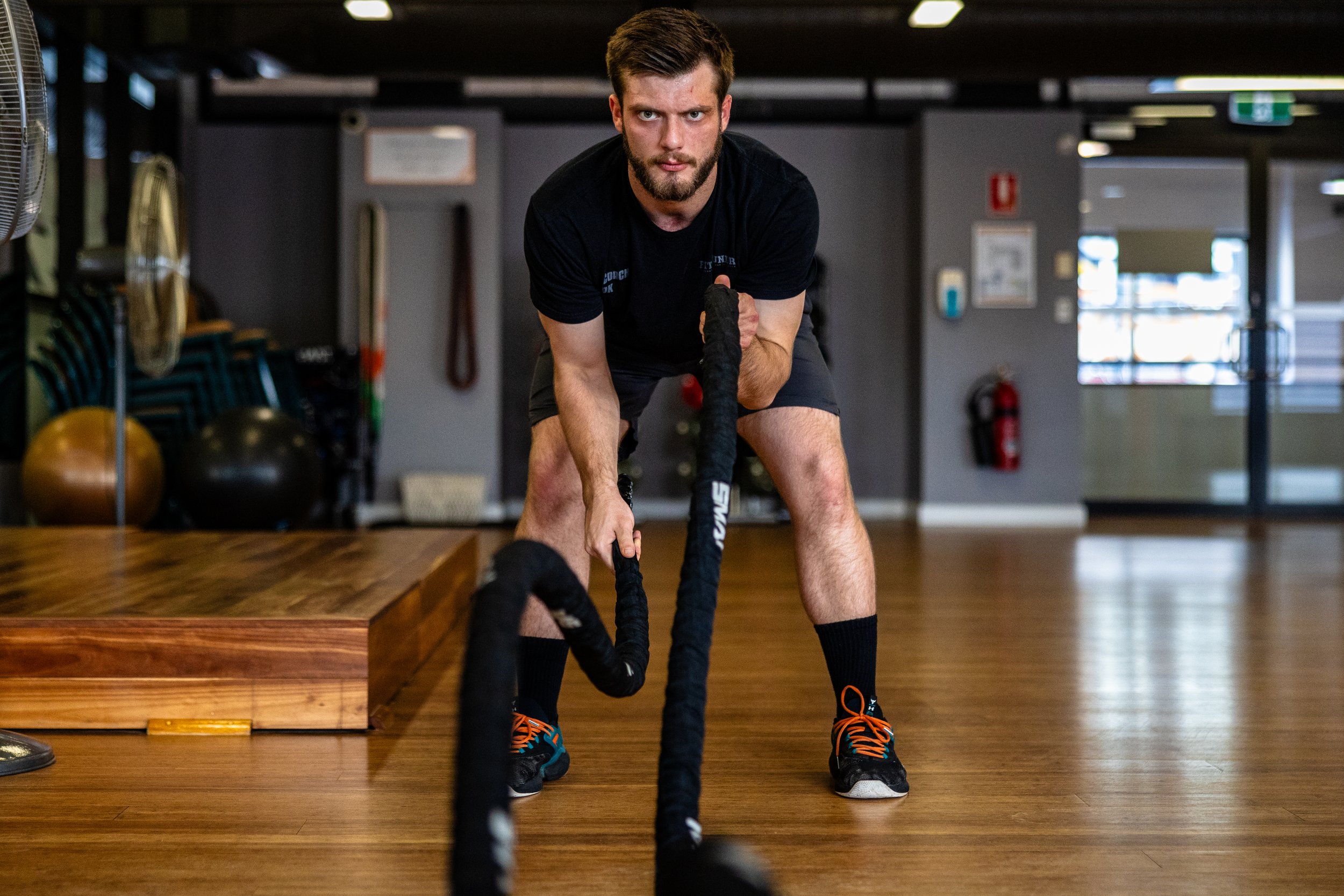 Man in a gym pulling on battle ropes during workout.
