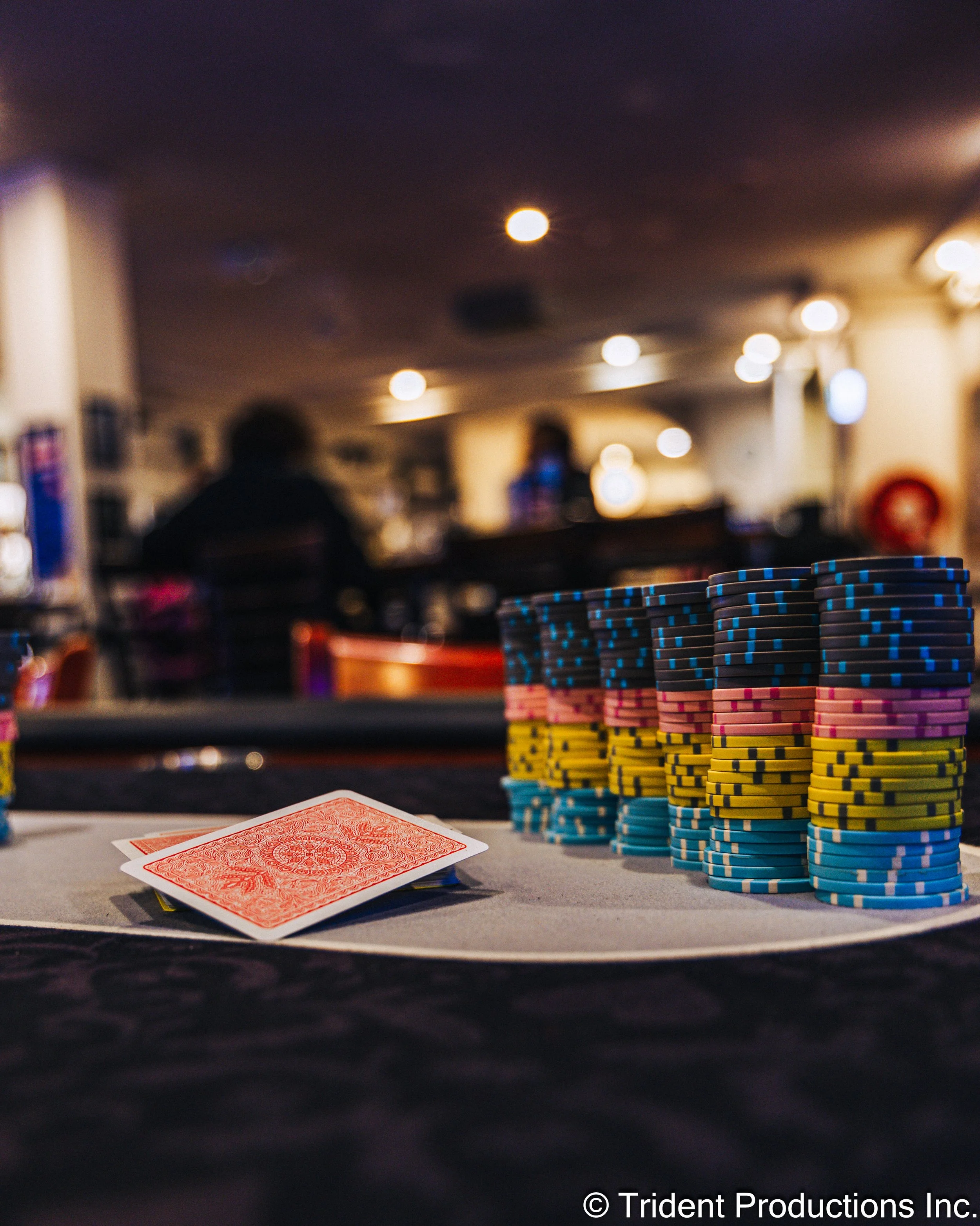 Poker chips stacked on a table with a playing card in the foreground at a poker game in a dimly lit casino or poker room.
