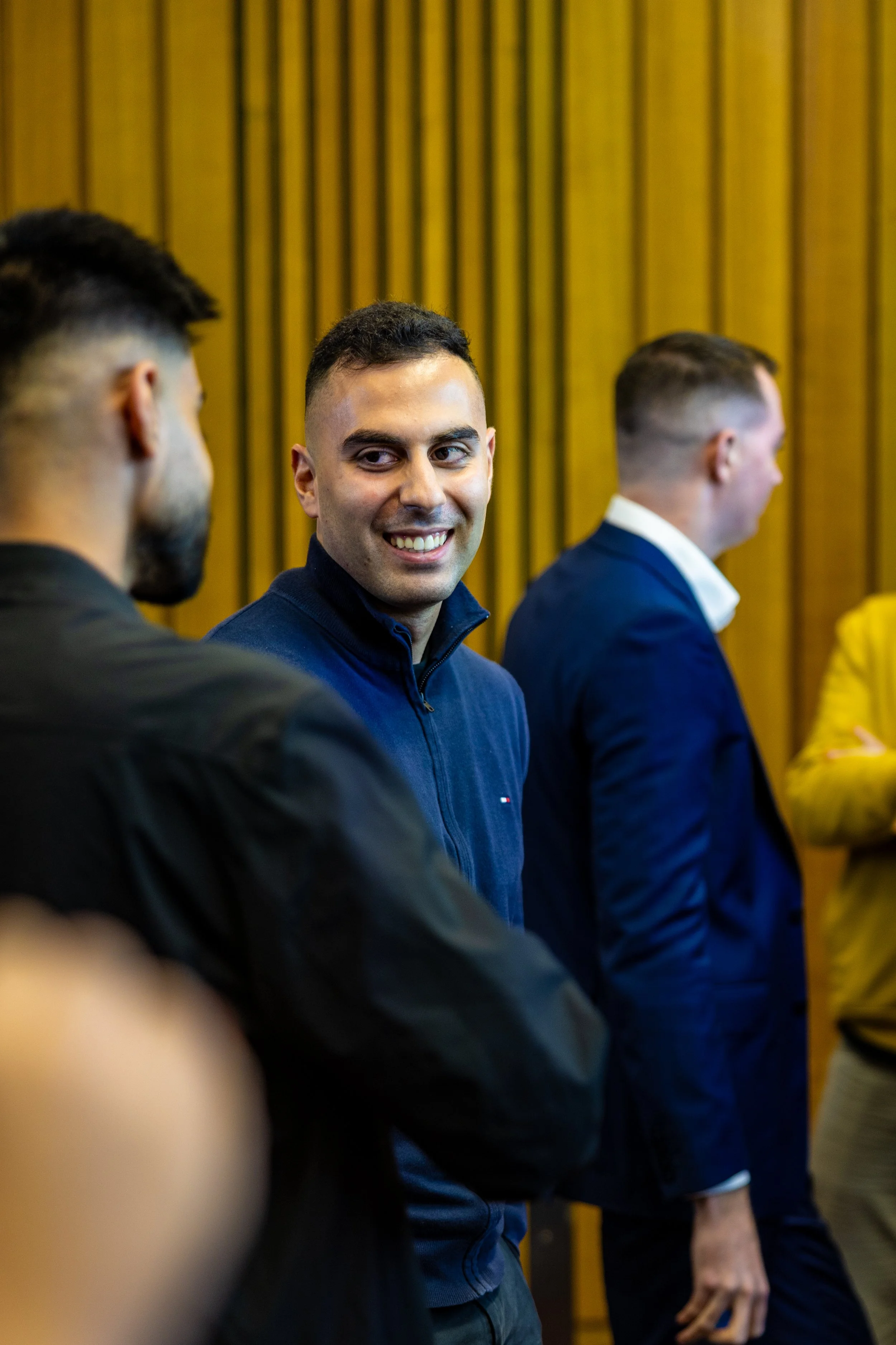 A group of men talking in a professional setting with Wood-paneled walls.