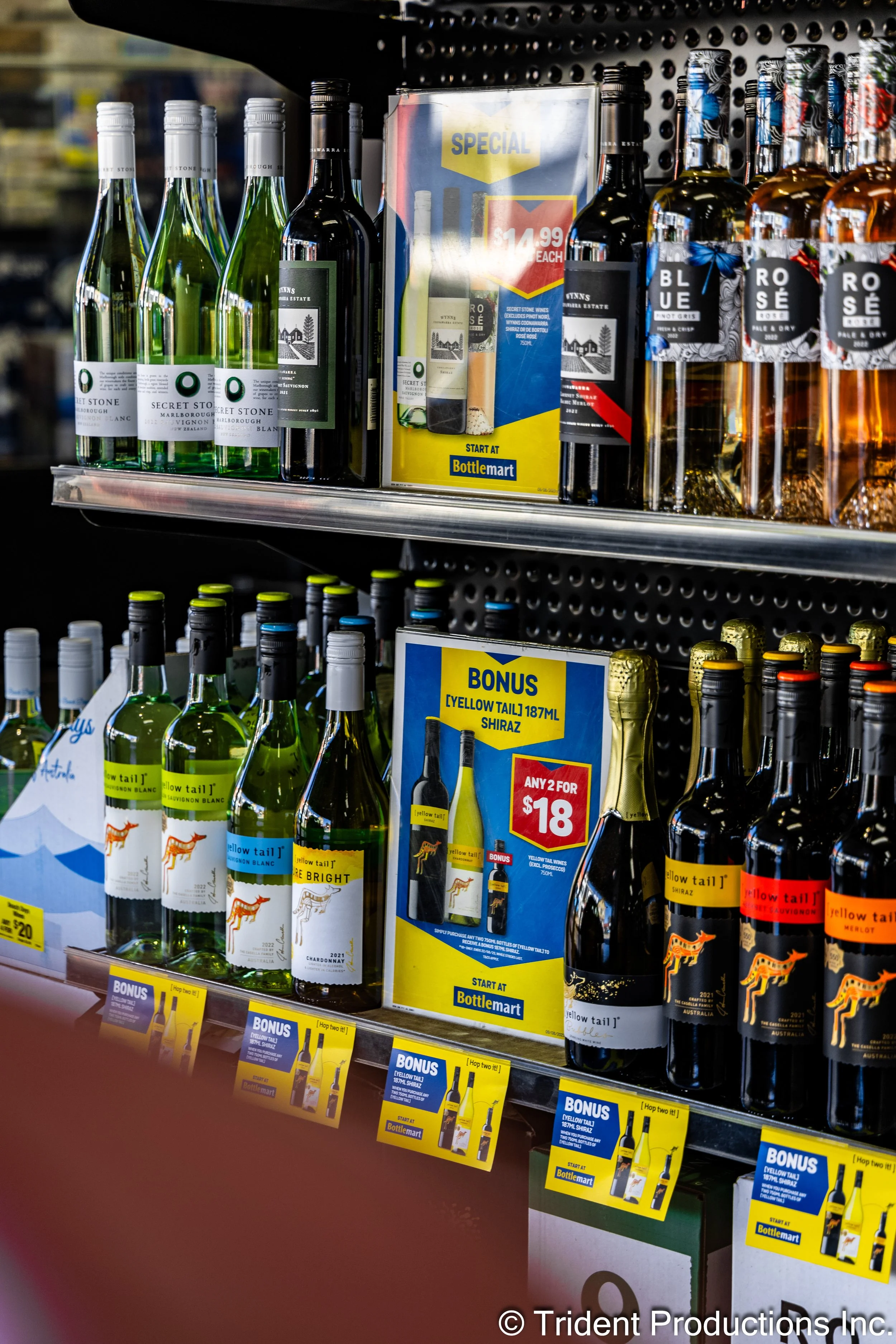 Shelf display of various wine bottles at a store, with promotional signs advertising special prices, bonuses, and discounts.