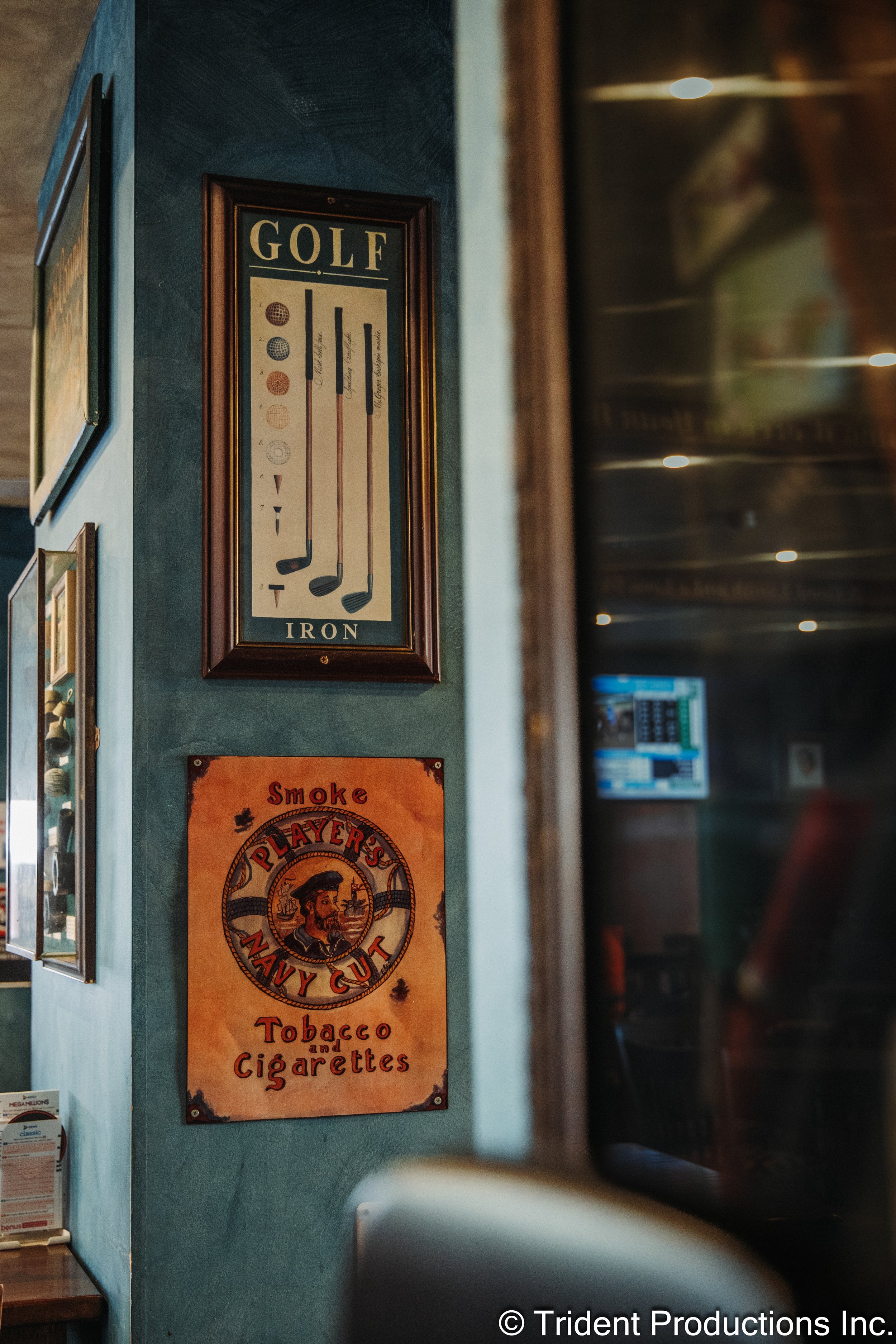 Decorative posters on a teal wall, including one with golf clubs and the words "GOLF IRON" and another with a vintage design for tobacco and cigarettes by Smoke Player's Navy Cut.