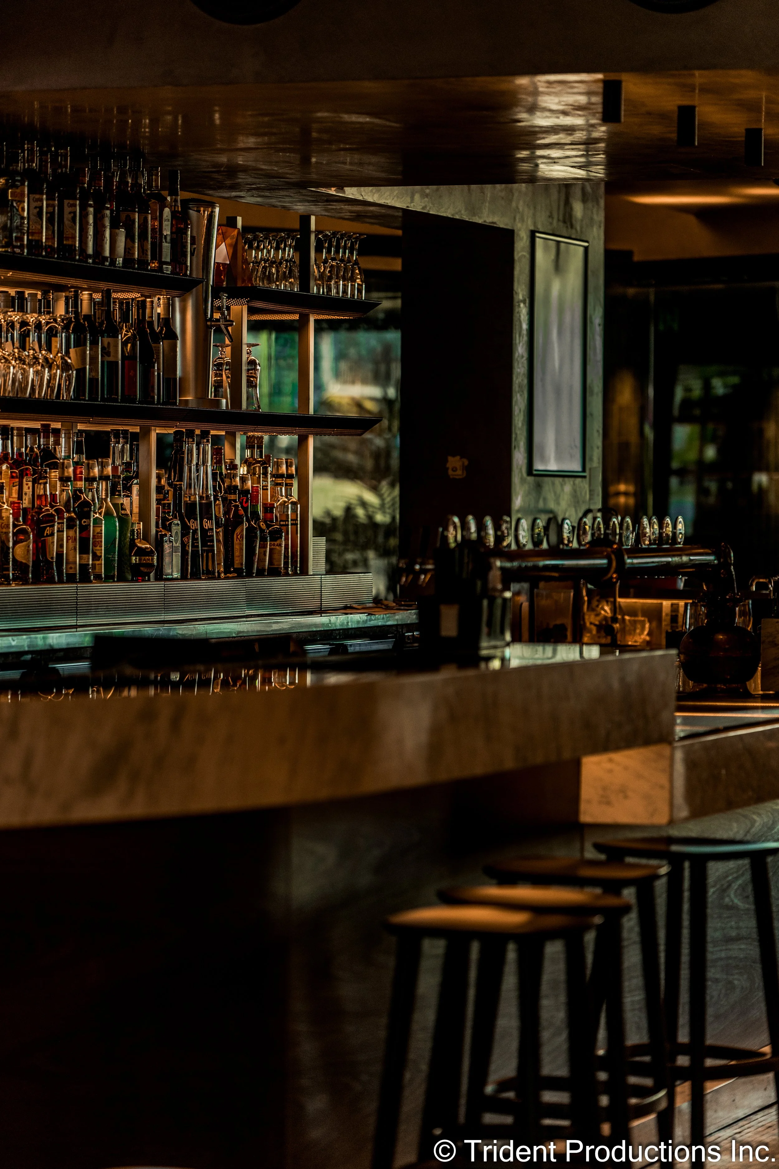 Empty bar with bottles of alcohol on shelves, dark interior, and bar stools lined up.