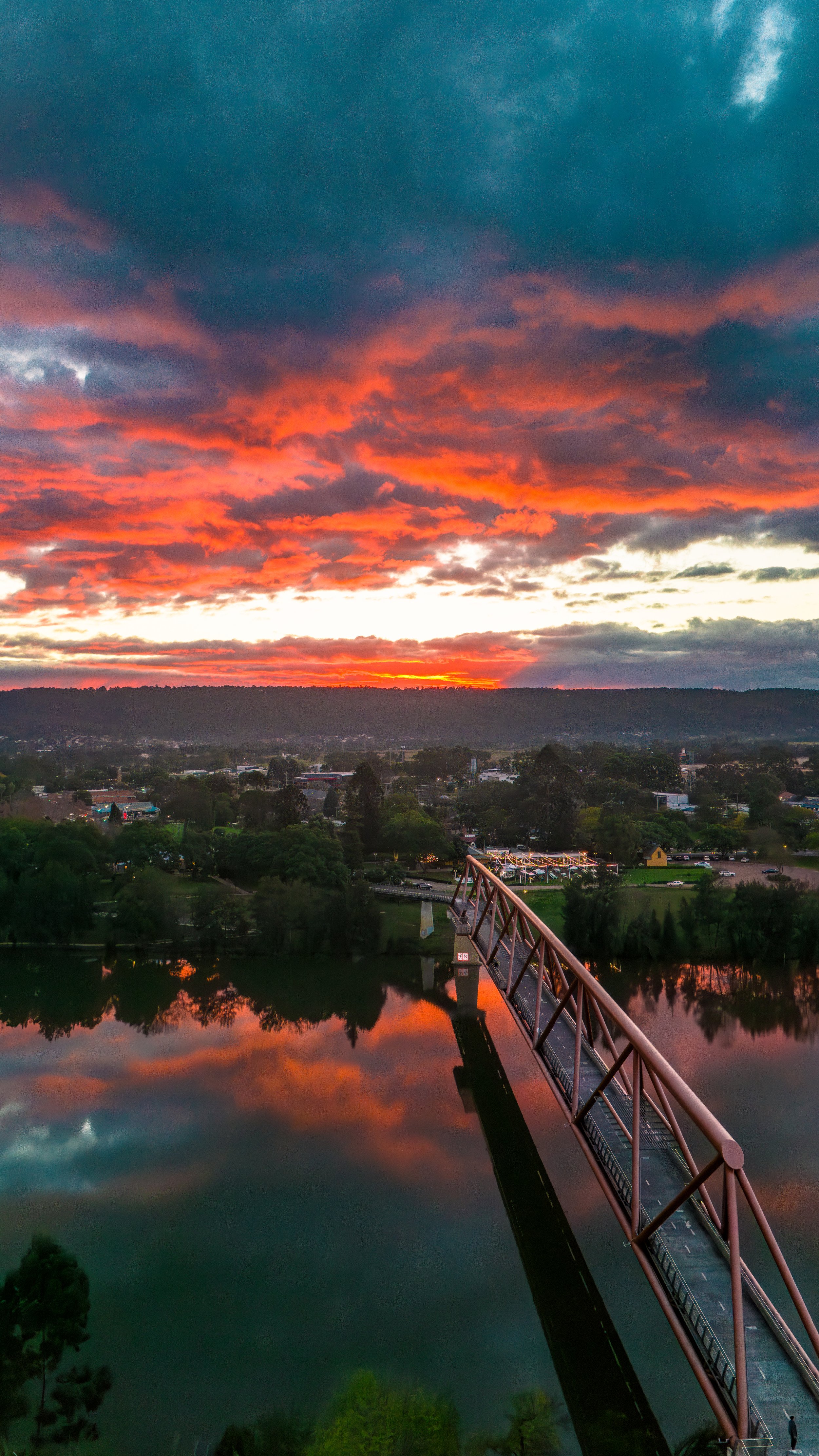 Sunset over a river with a bridge extending into the distance, reflecting vibrant orange and blue colors in the water and sky.