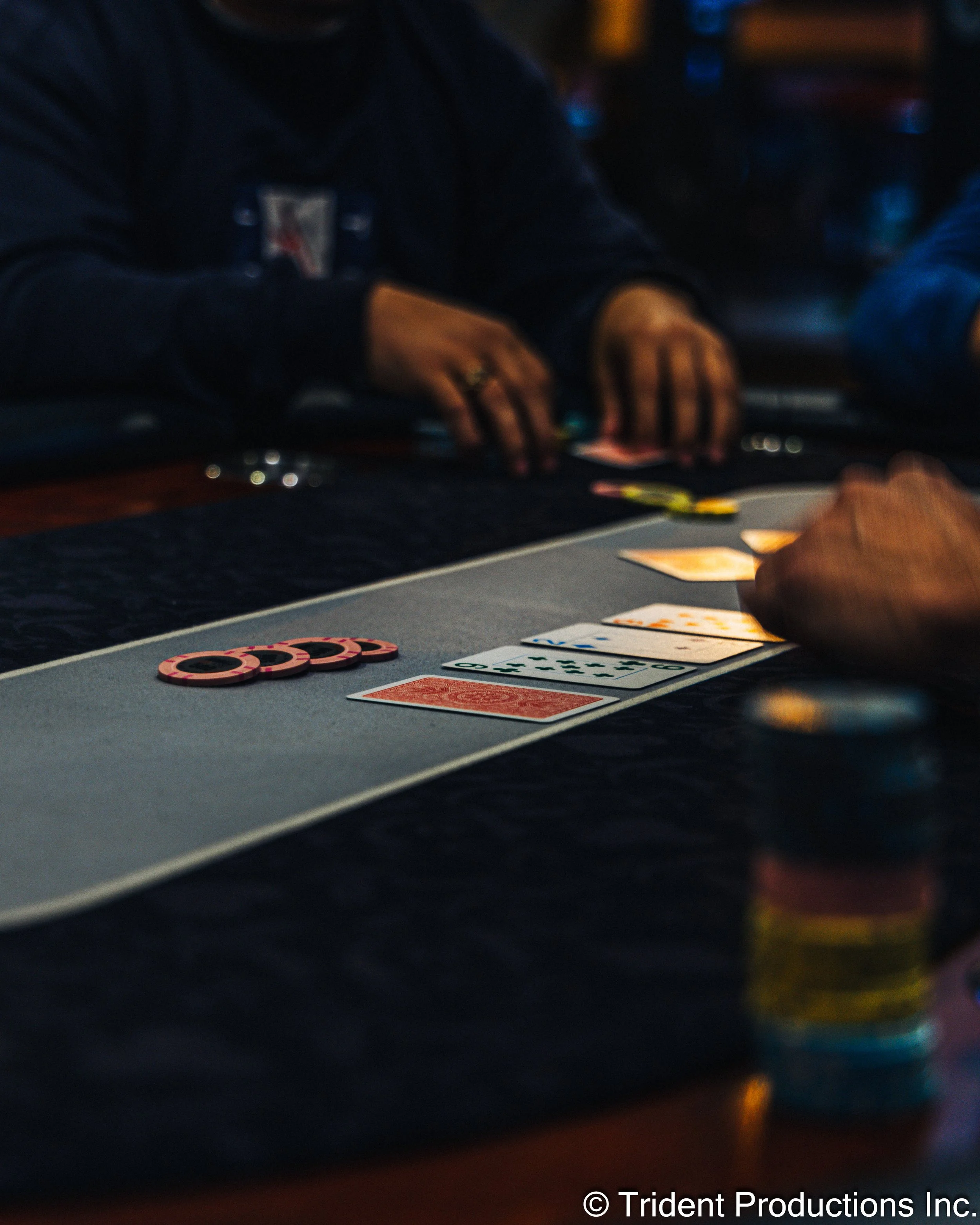 People playing poker at a casino table, with playing cards, poker chips, and gambling tokens visible.