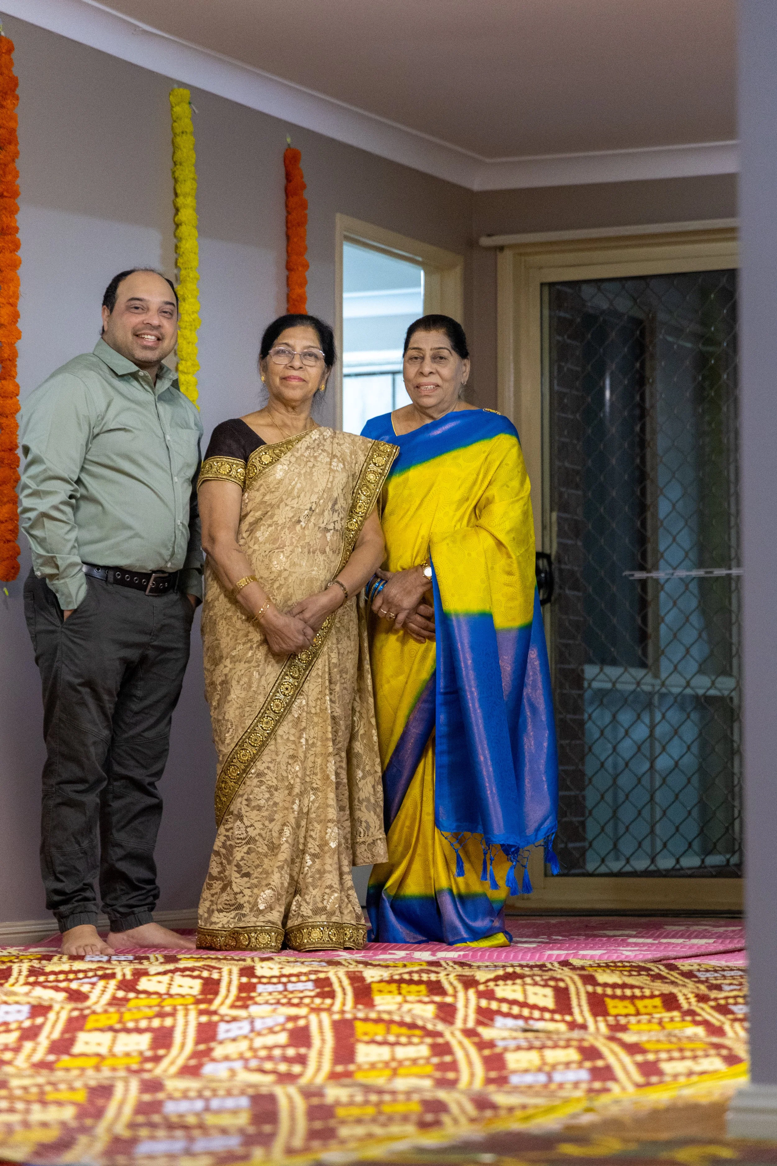 Four people standing together indoors at a celebration, with colorful hanging decorations on the wall.