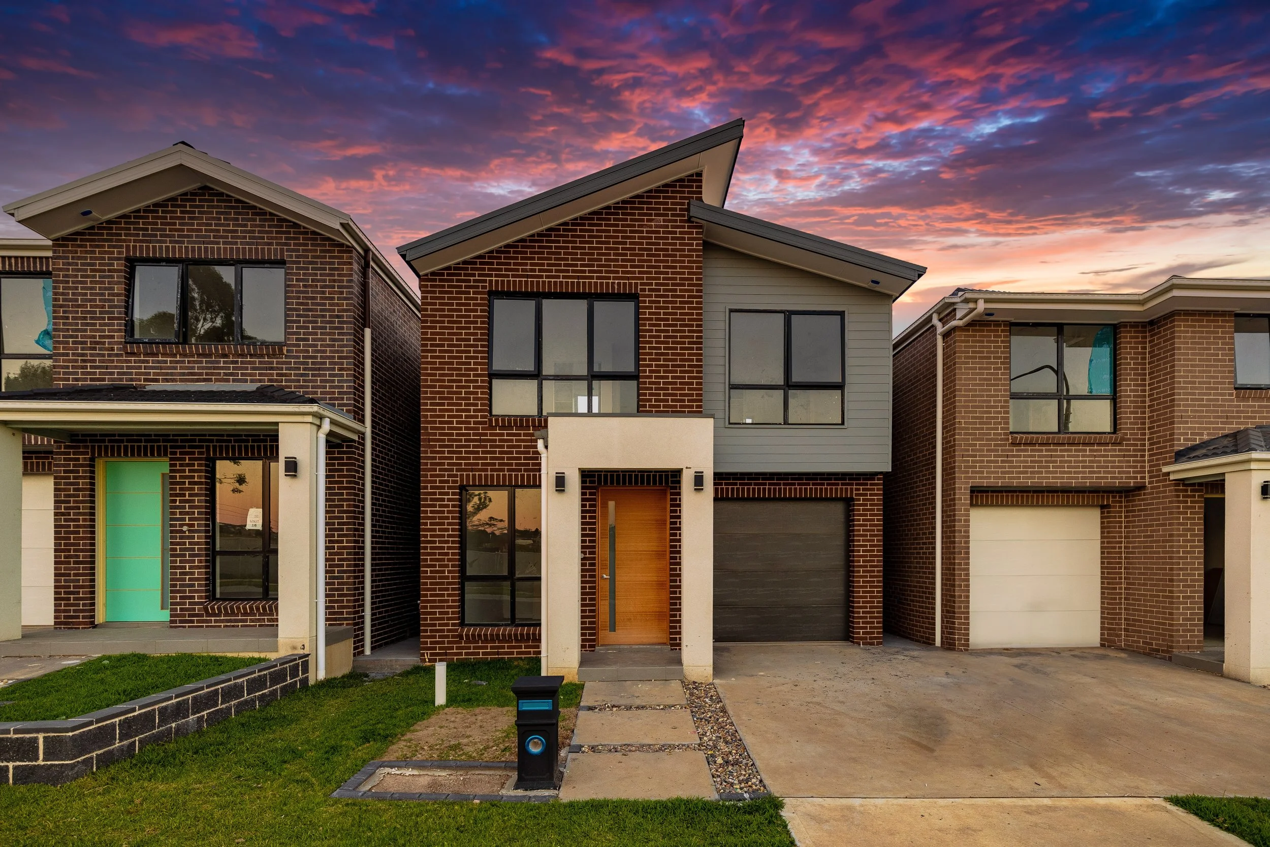 Modern brick house with a unique angled roof, large window, wooden front door, and an attached garage, set against a sunset sky.