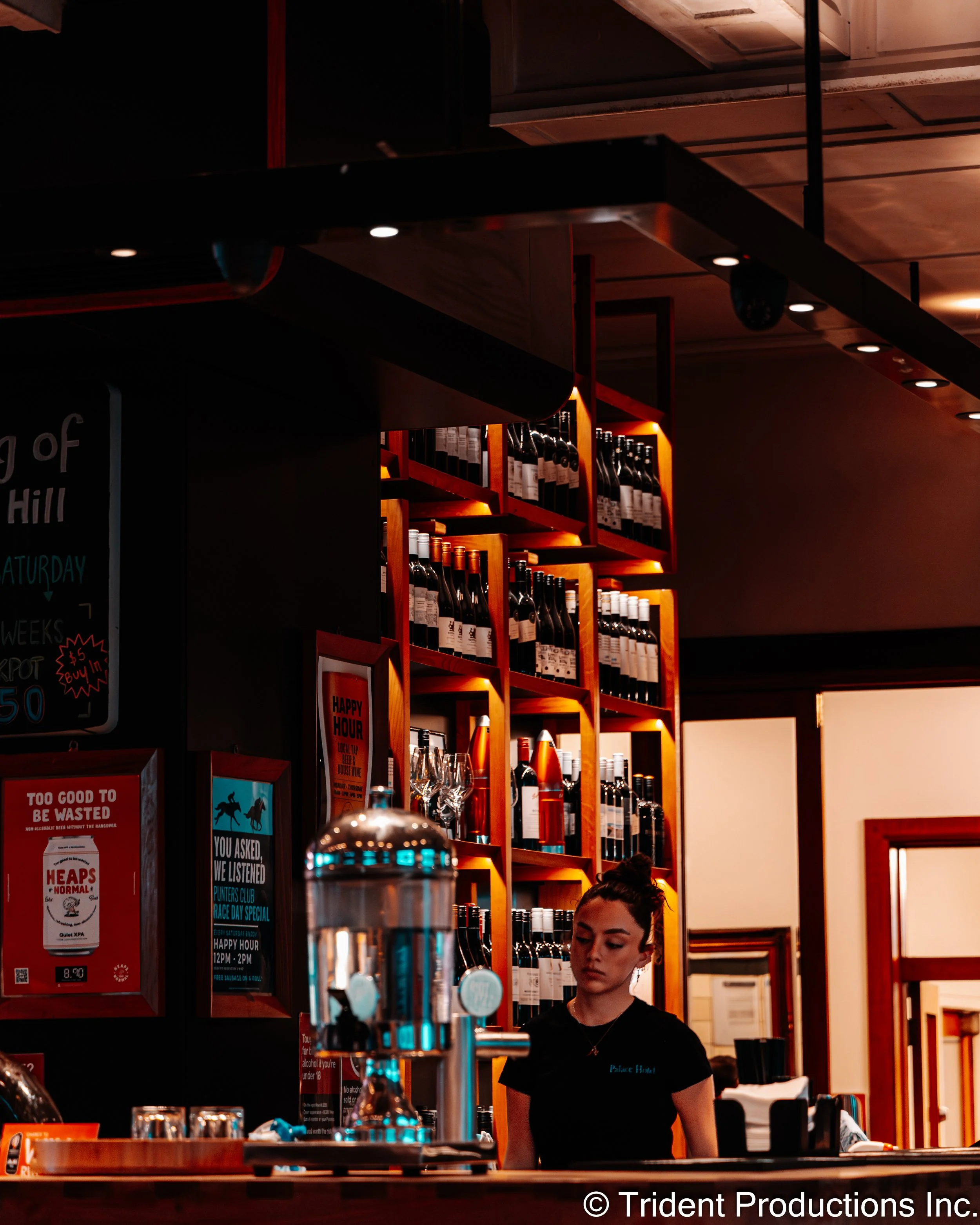Bar with a bartender standing behind the counter, shelves filled with wine bottles, and promotional posters on the wall.