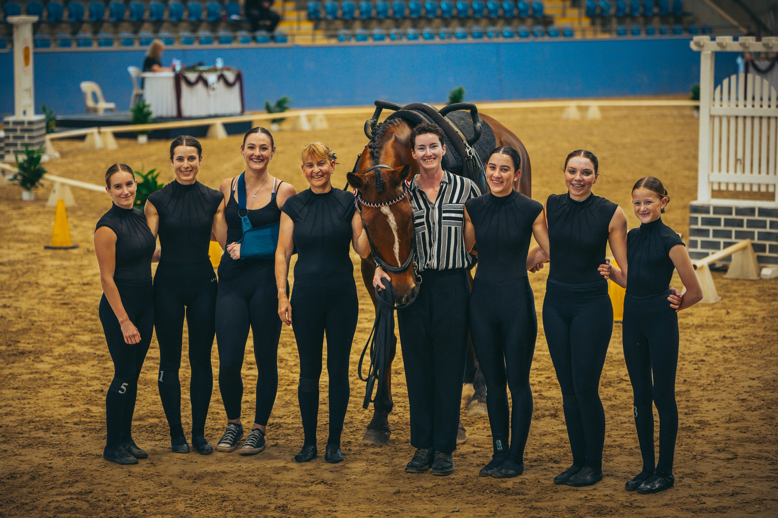 Group of women and a girl standing with a palace in the background and a horse at an indoor equestrian arena.