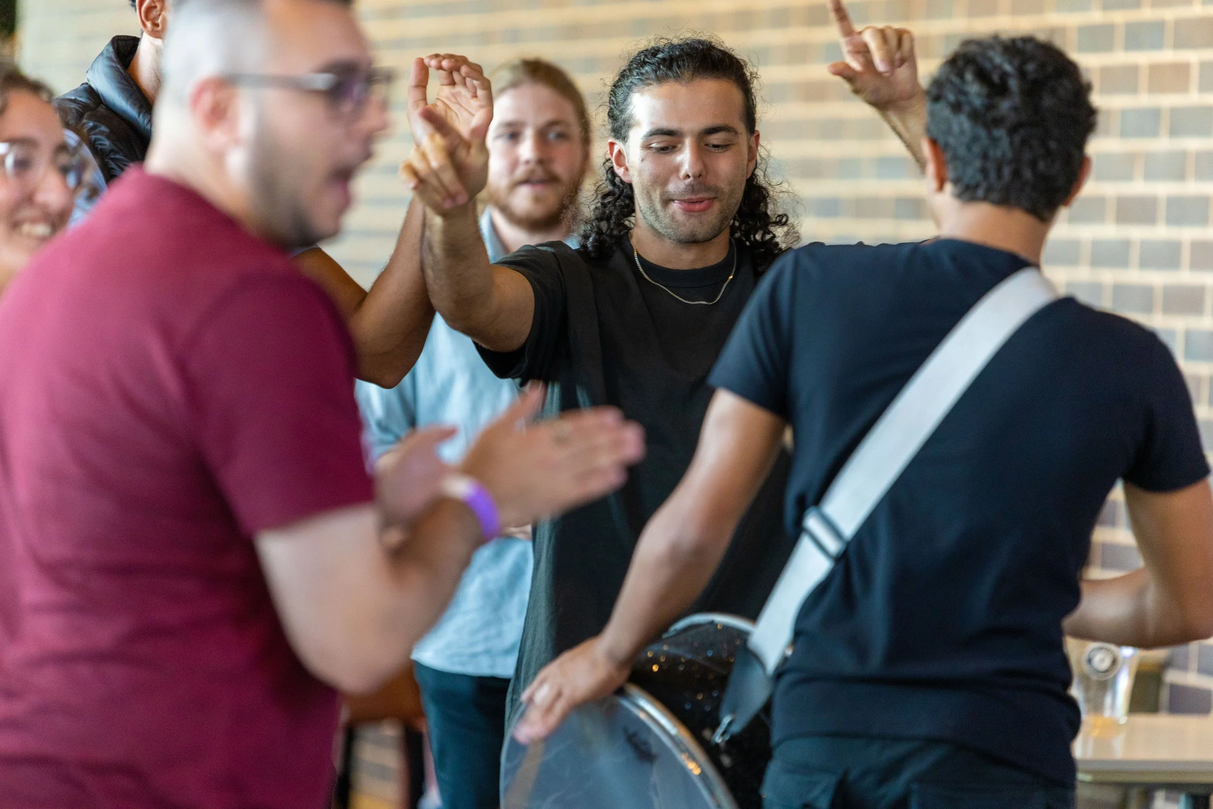 Group of young people at a social gathering, with one person playing a drum, others clapping and enjoying themselves.
