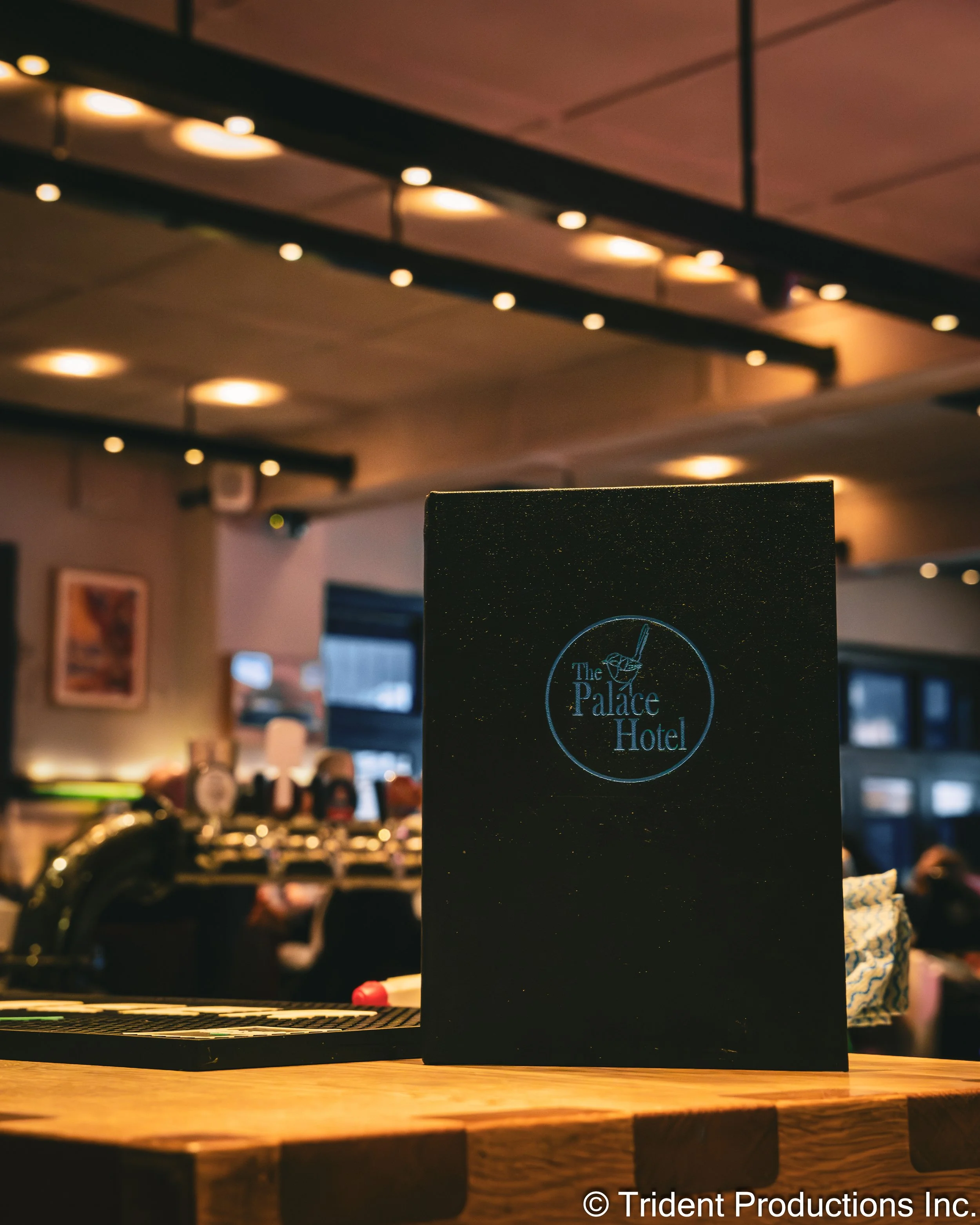 Menu or promotional booklet from The Palace Hotel on a wooden table in a dimly lit bar or restaurant.
