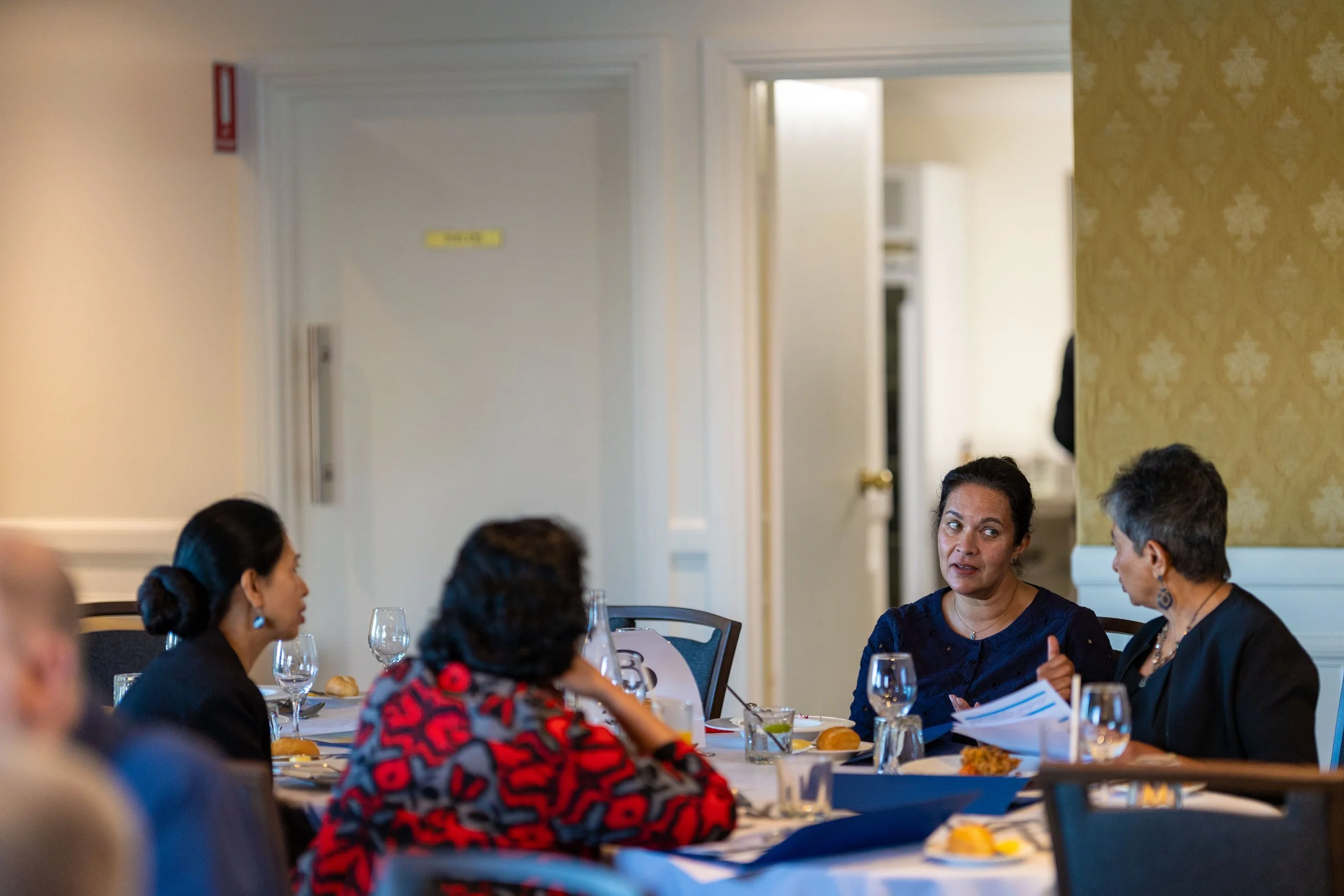 A group of women sitting at a dining table and engaging in conversation during a formal event or dinner.