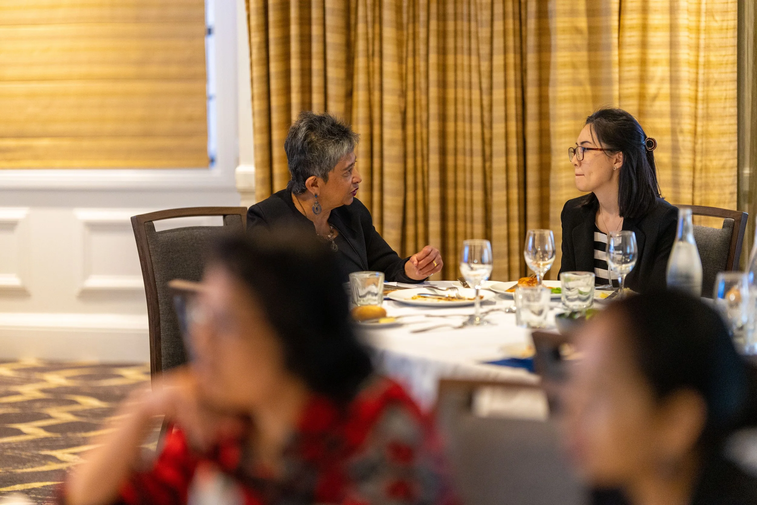 Two women sitting at a round dining table having a conversation at a formal event.