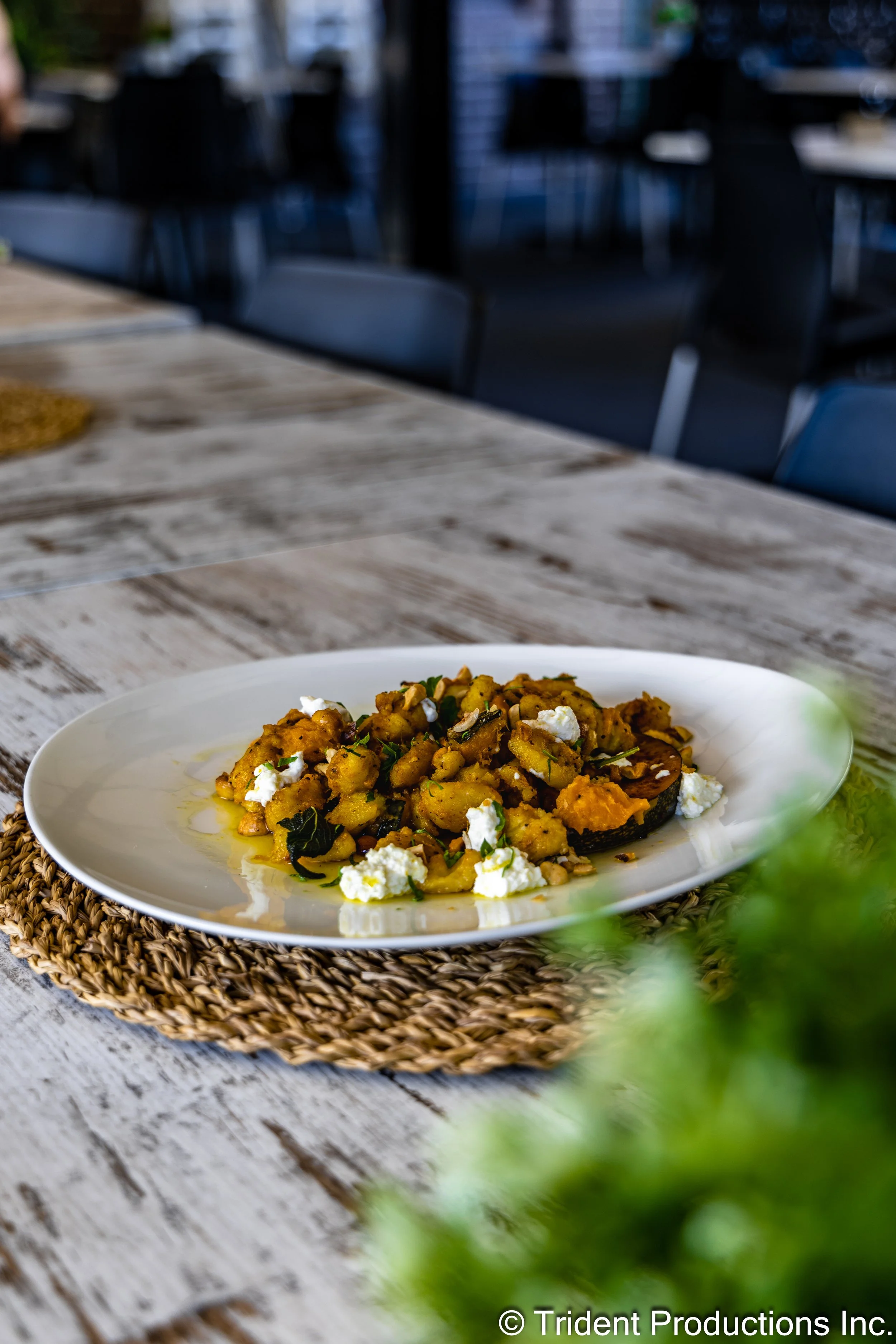Plate of scrambled eggs with herbs and crumbled cheese, on a rustic wooden table in a dining area.