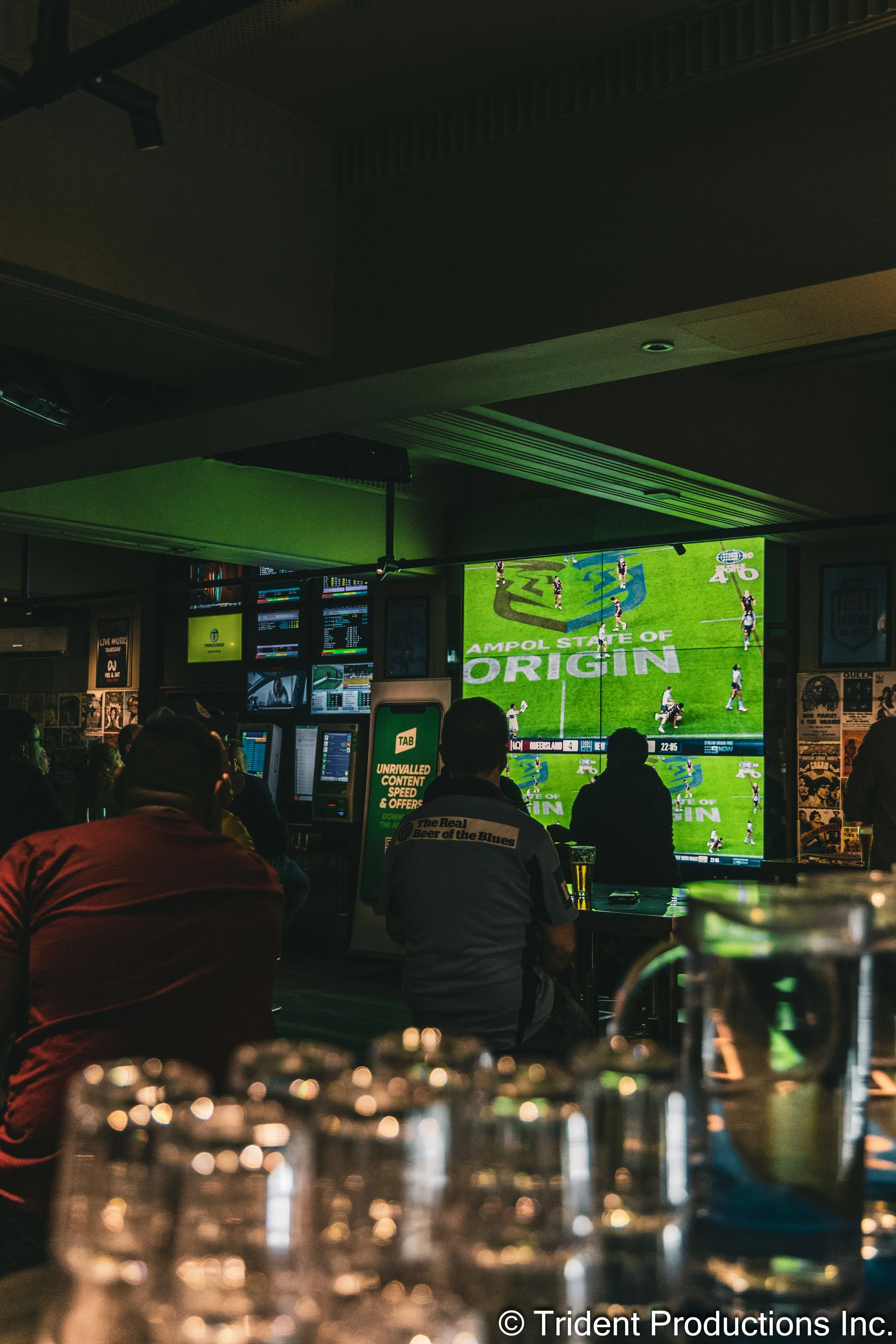 People watching a rugby match on large screens in a dimly lit bar or pub.