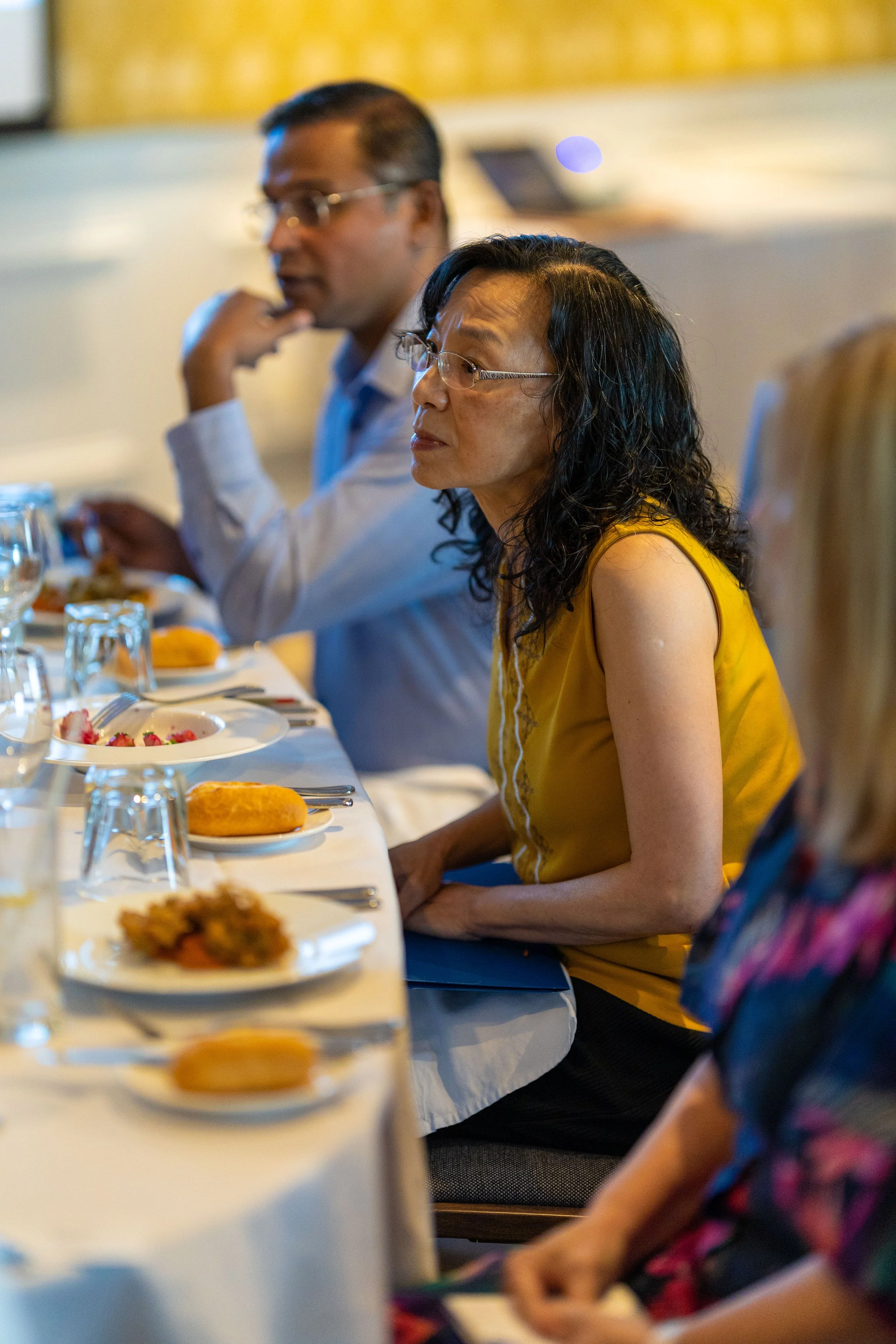 People sitting at a dining table during a formal meal, with plates of food, glasses, and utensils.
