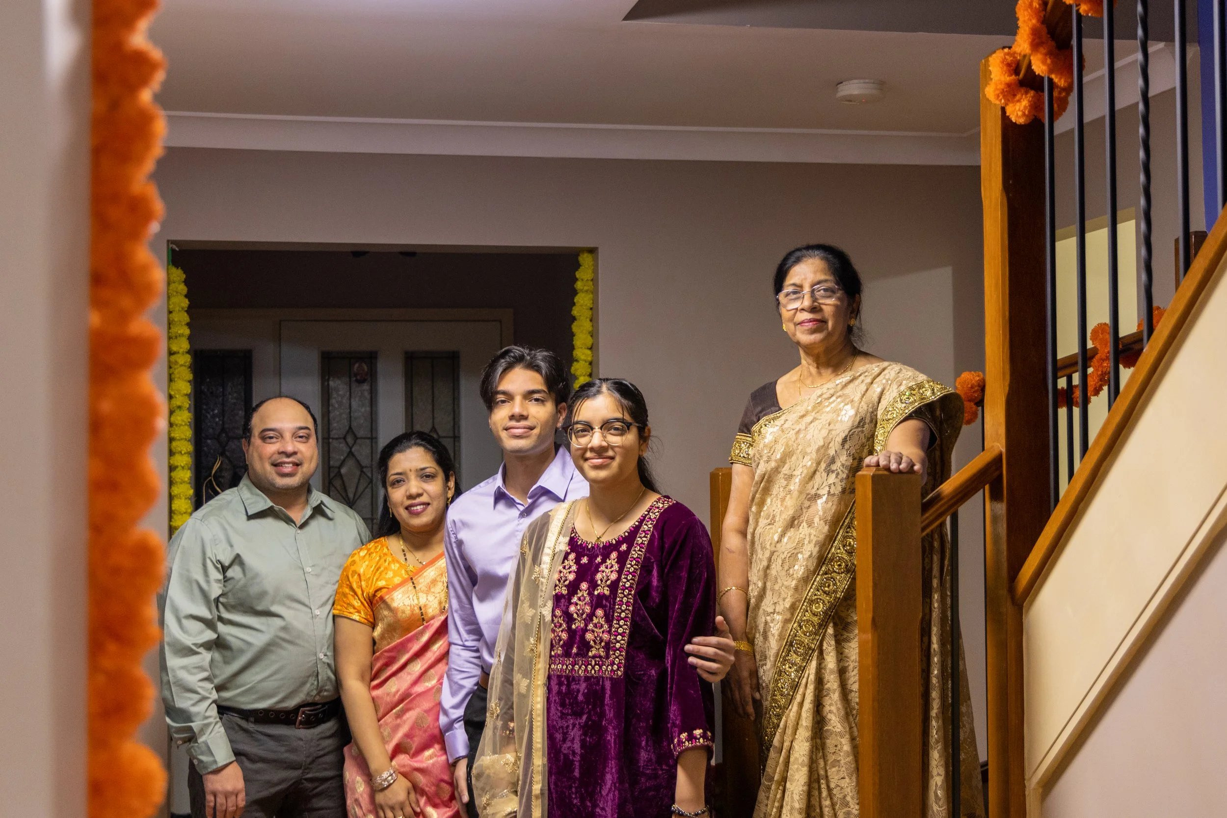 Family of six standing on staircase at home, dressed in traditional Indian attire for celebration.
