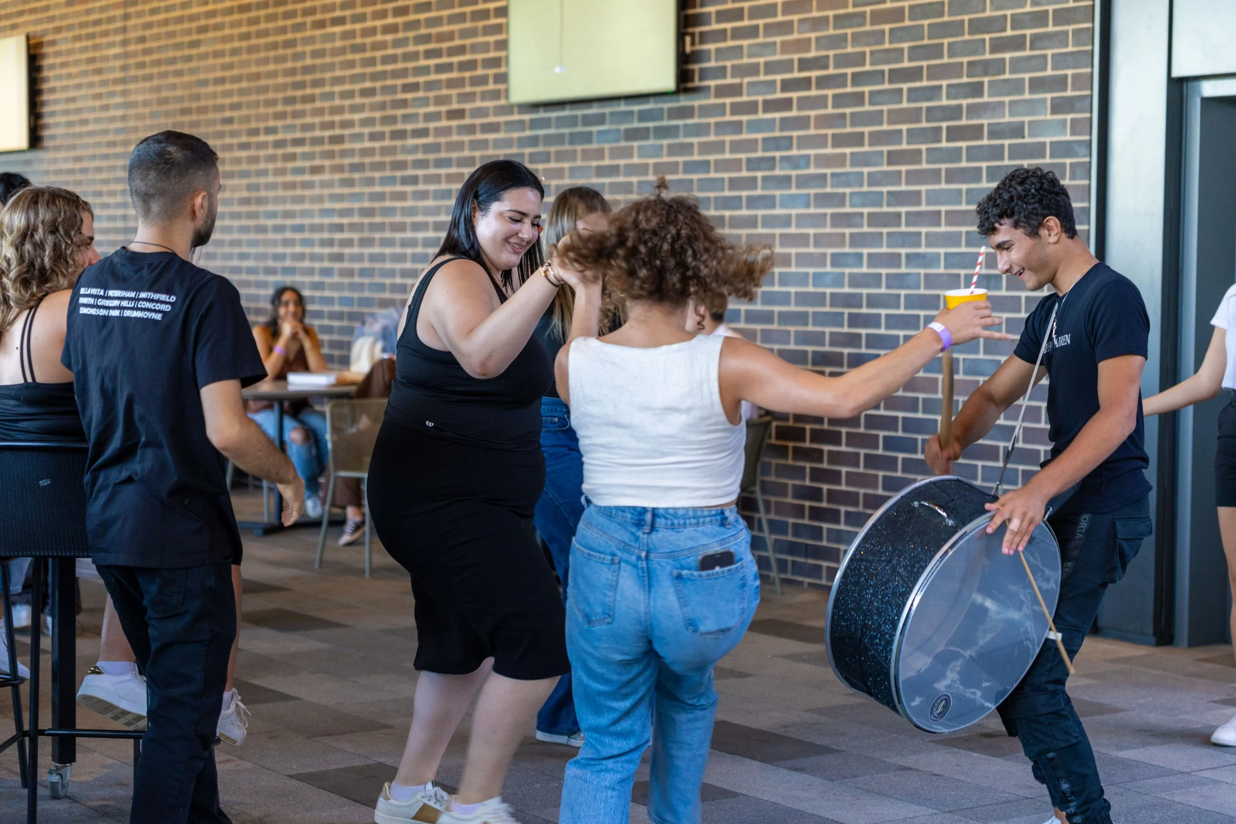 People dancing and playing musical instruments at an indoor event with a brick wall background.