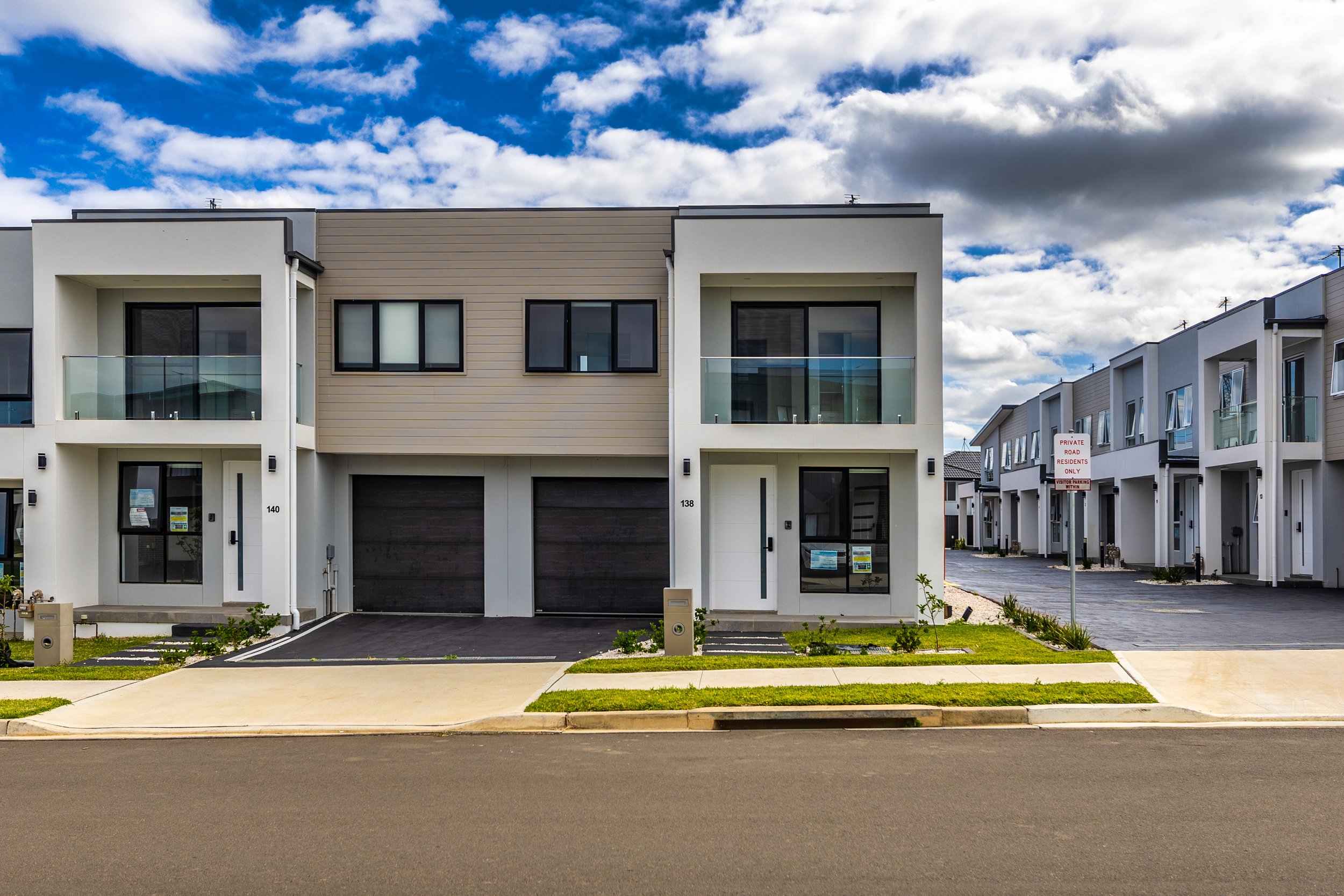 Modern residential townhouses with two stories, garages, and balconies, under a partly cloudy sky.