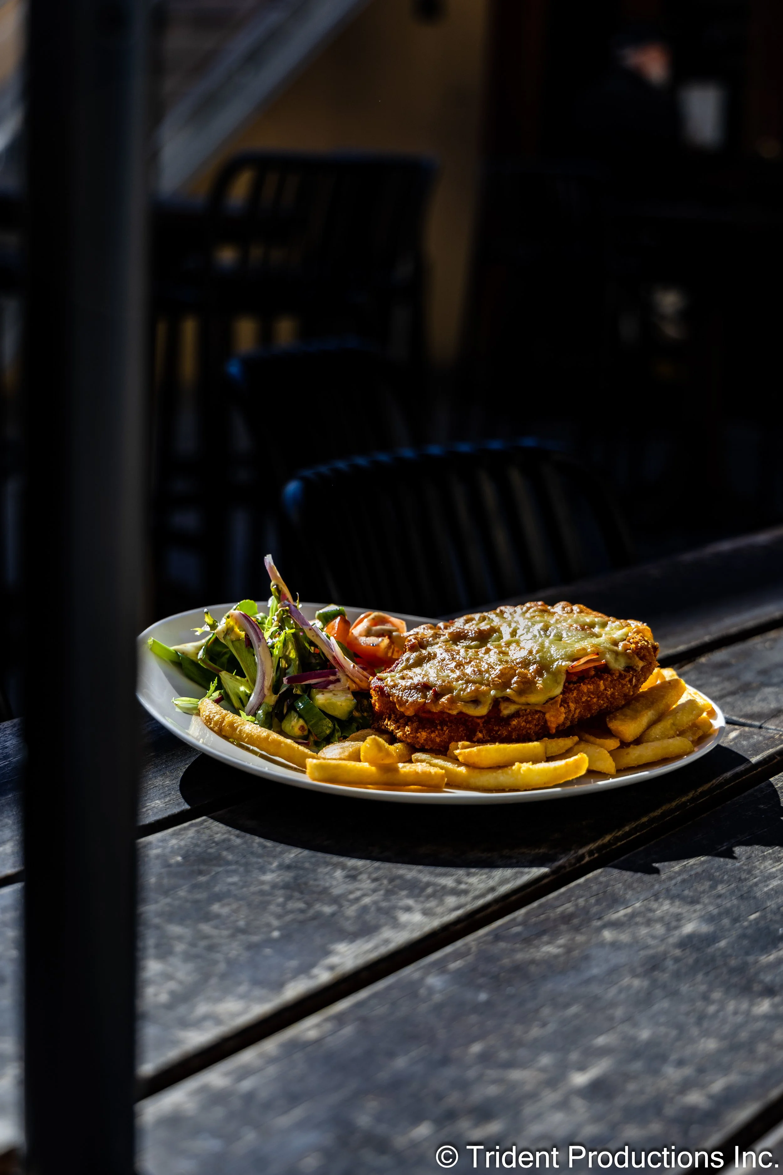 A plate of fried chicken with melted cheese, French fries, and a side salad with greens, purple onion, and carrots on a dark wooden table.