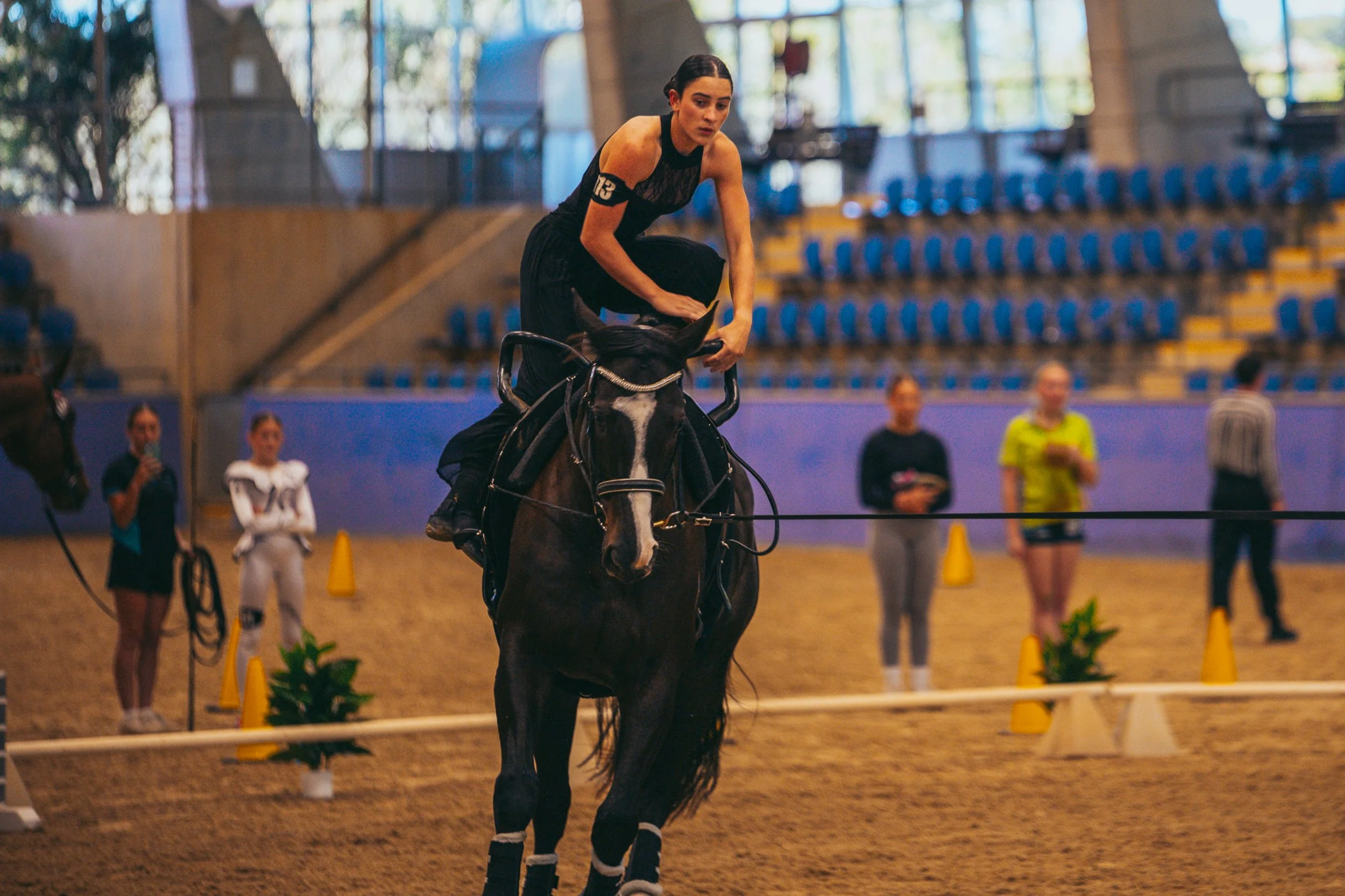 Female equestrian riding a horse in an indoor arena with spectators watching.