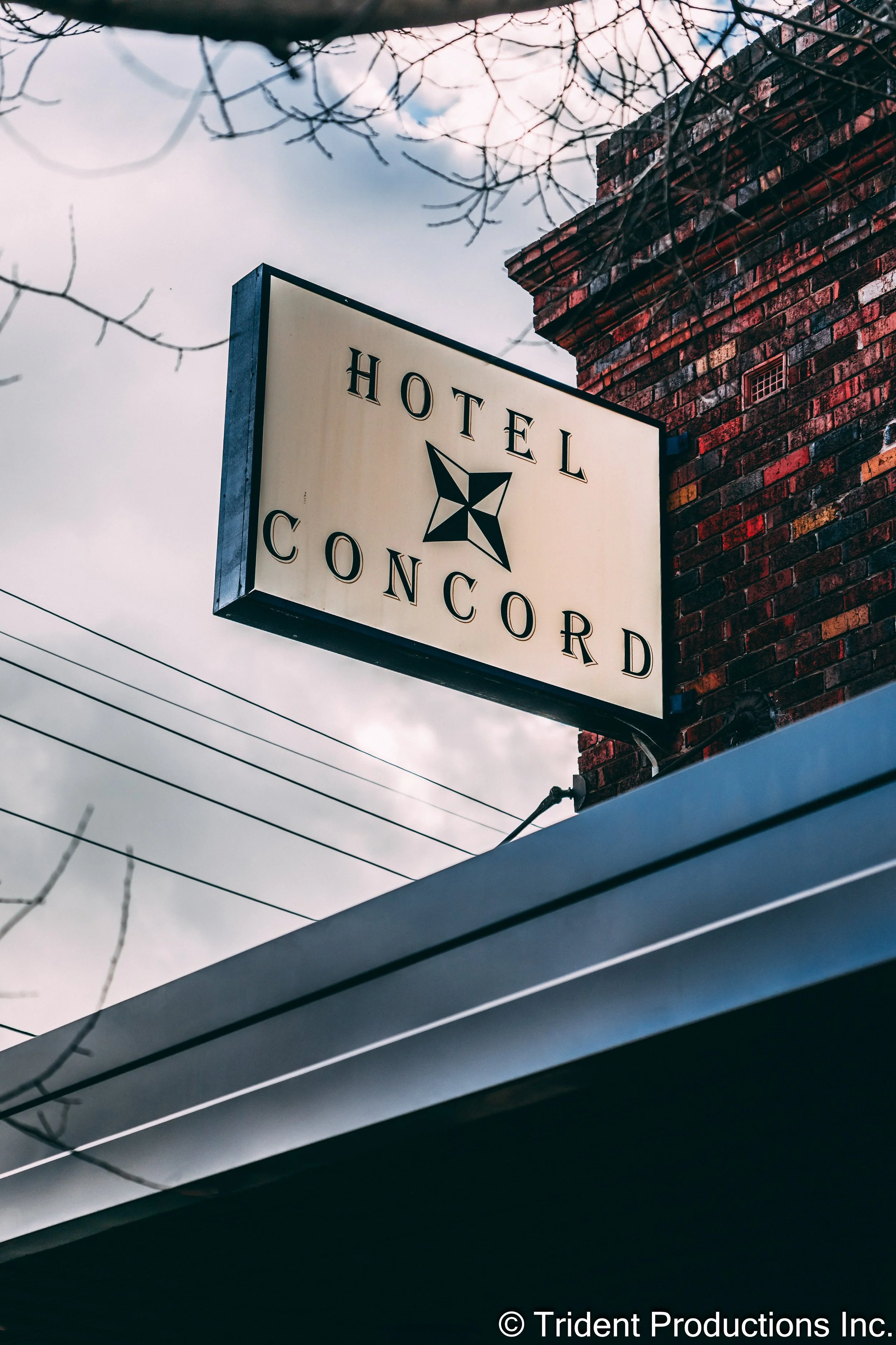 Sign for Hotel Concord mounted on a brick wall, with leafless tree branches and power lines visible in the background.