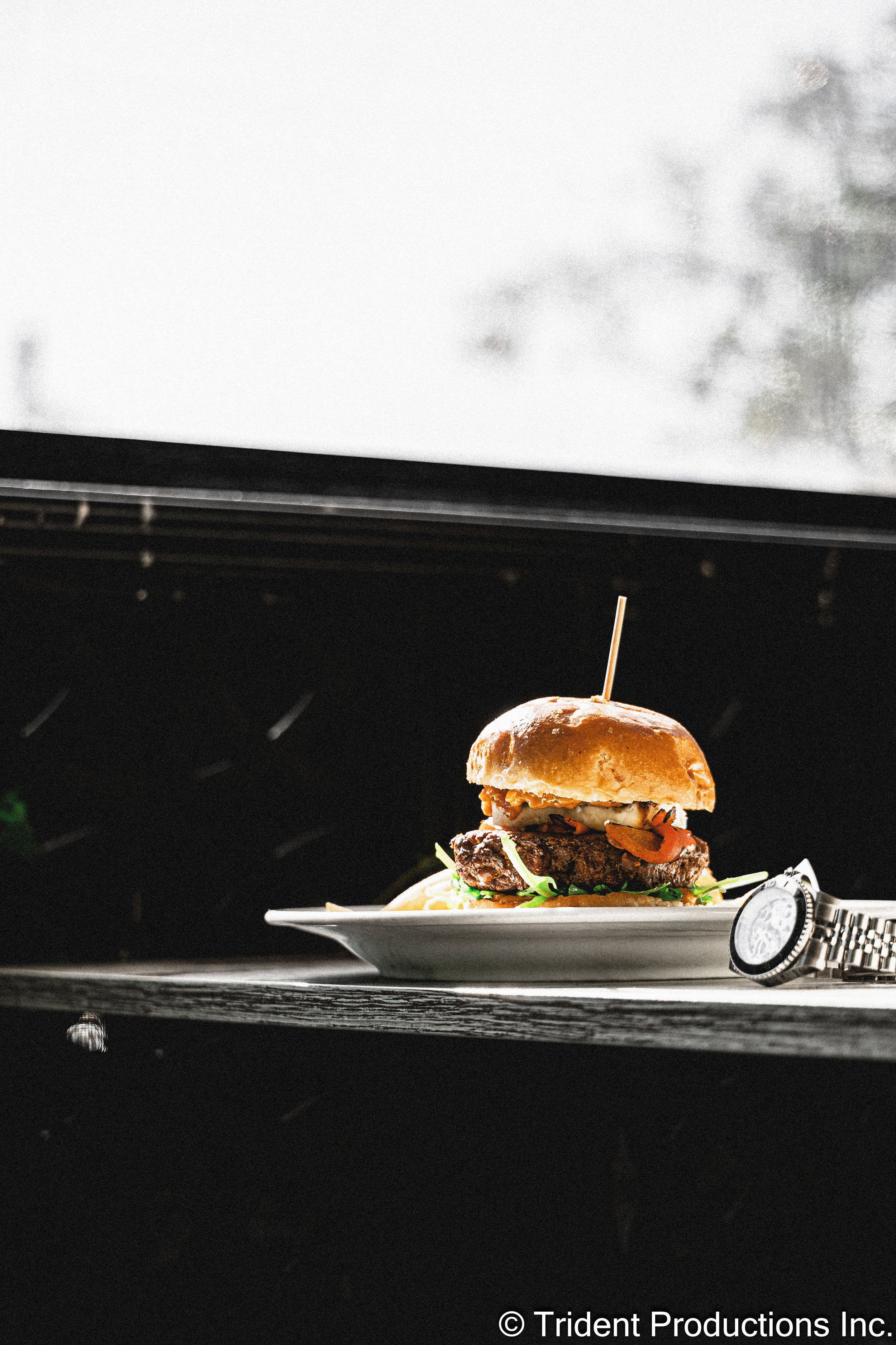 A plate with a cheeseburger and a watch on the side, placed in front of a microwave.