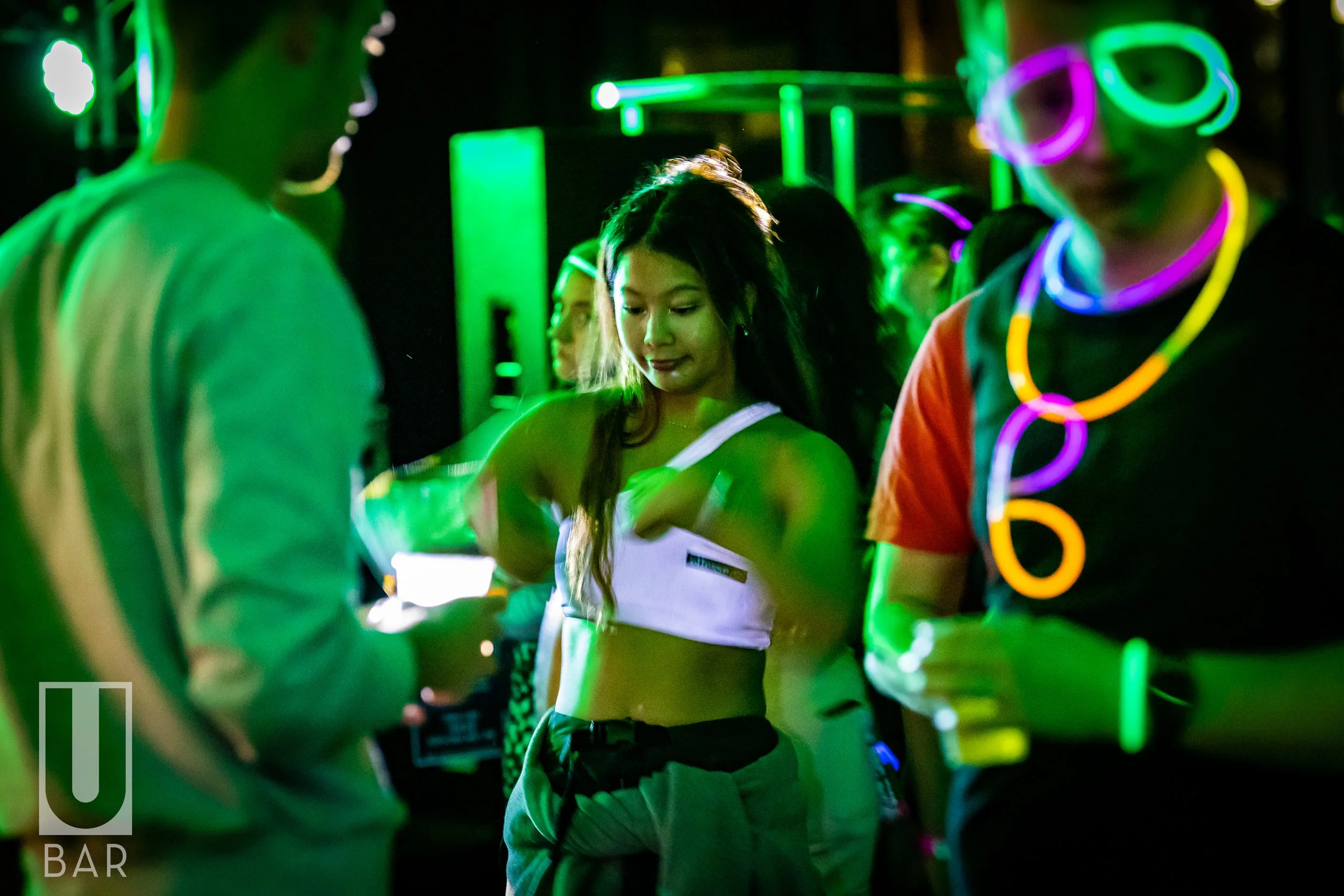 A group of young people at a neon-themed party, wearing glow-in-the-dark accessories and illuminated clothing, with colorful lighting and decorations.