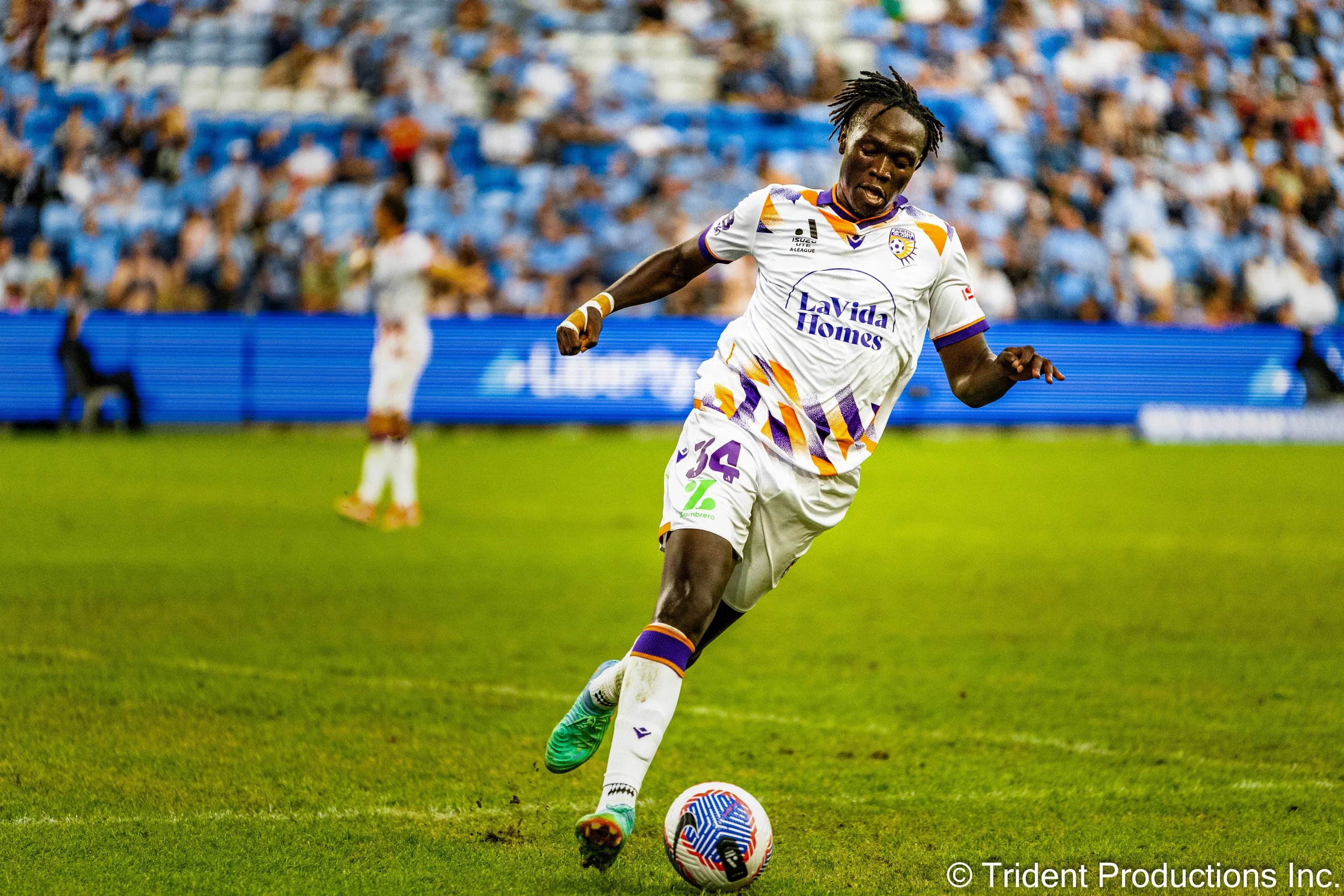 A soccer player in a white and purple uniform kicking a soccer ball on the field during a game.