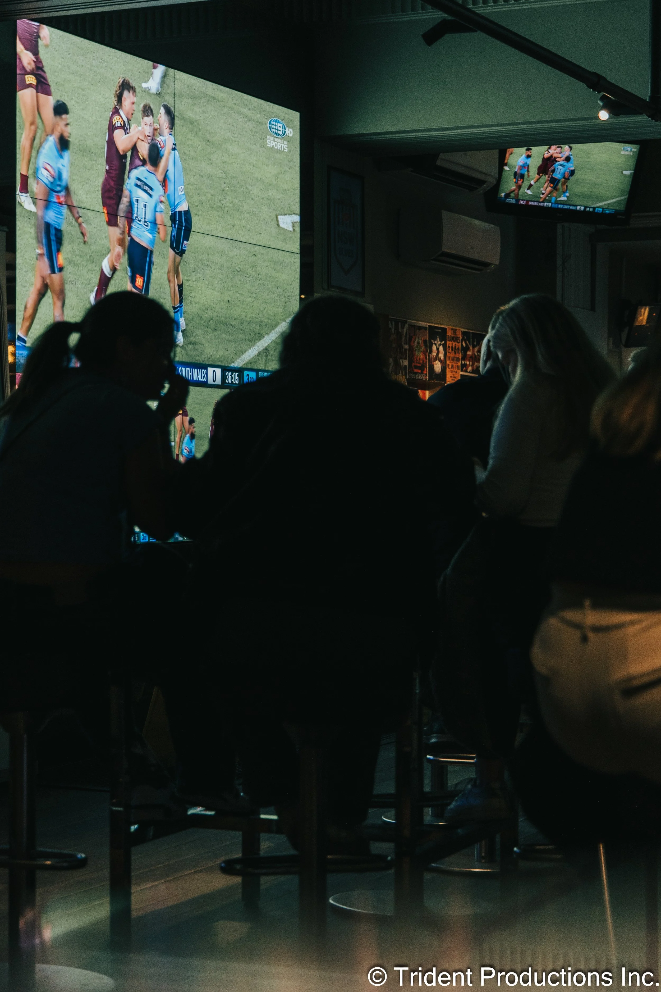 People watching a sports game on large television screens in a dimly lit bar or sports lounge.