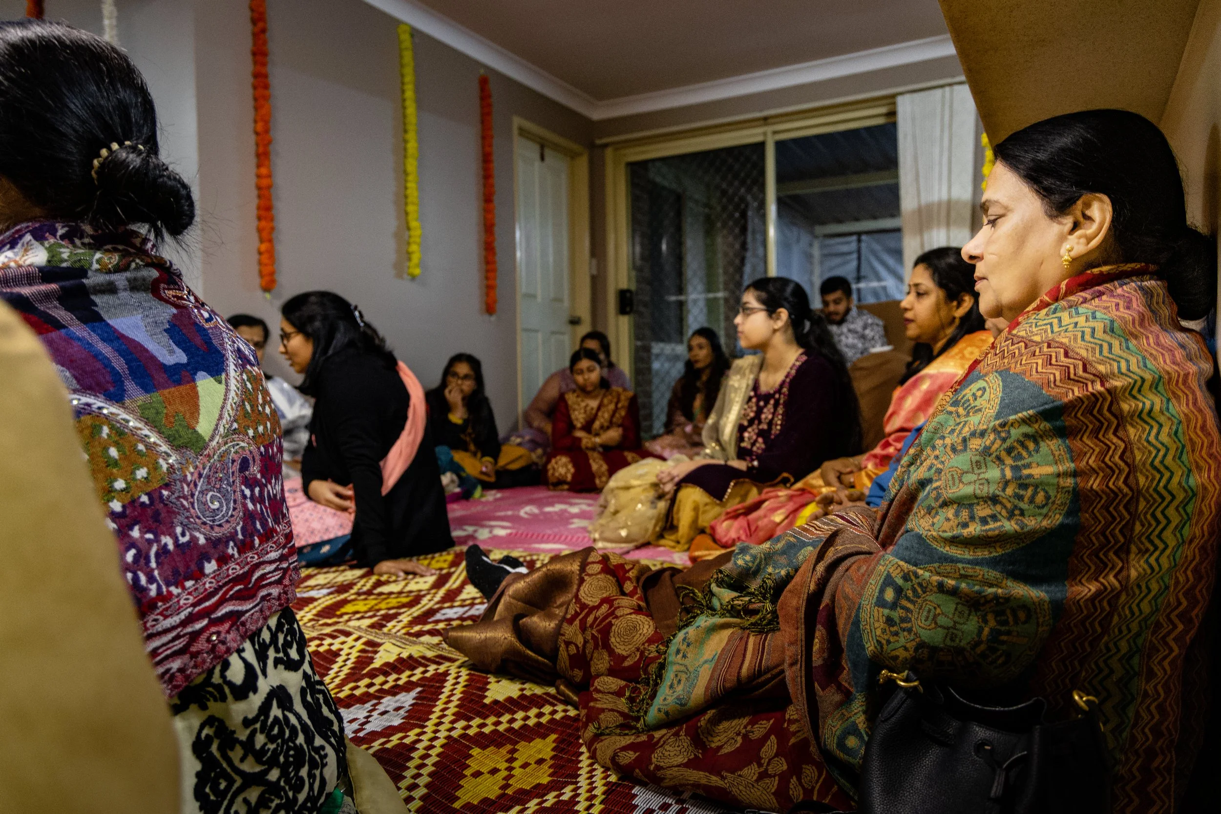 Group of women seated on the floor in traditional Indian attire during a religious or cultural gathering.