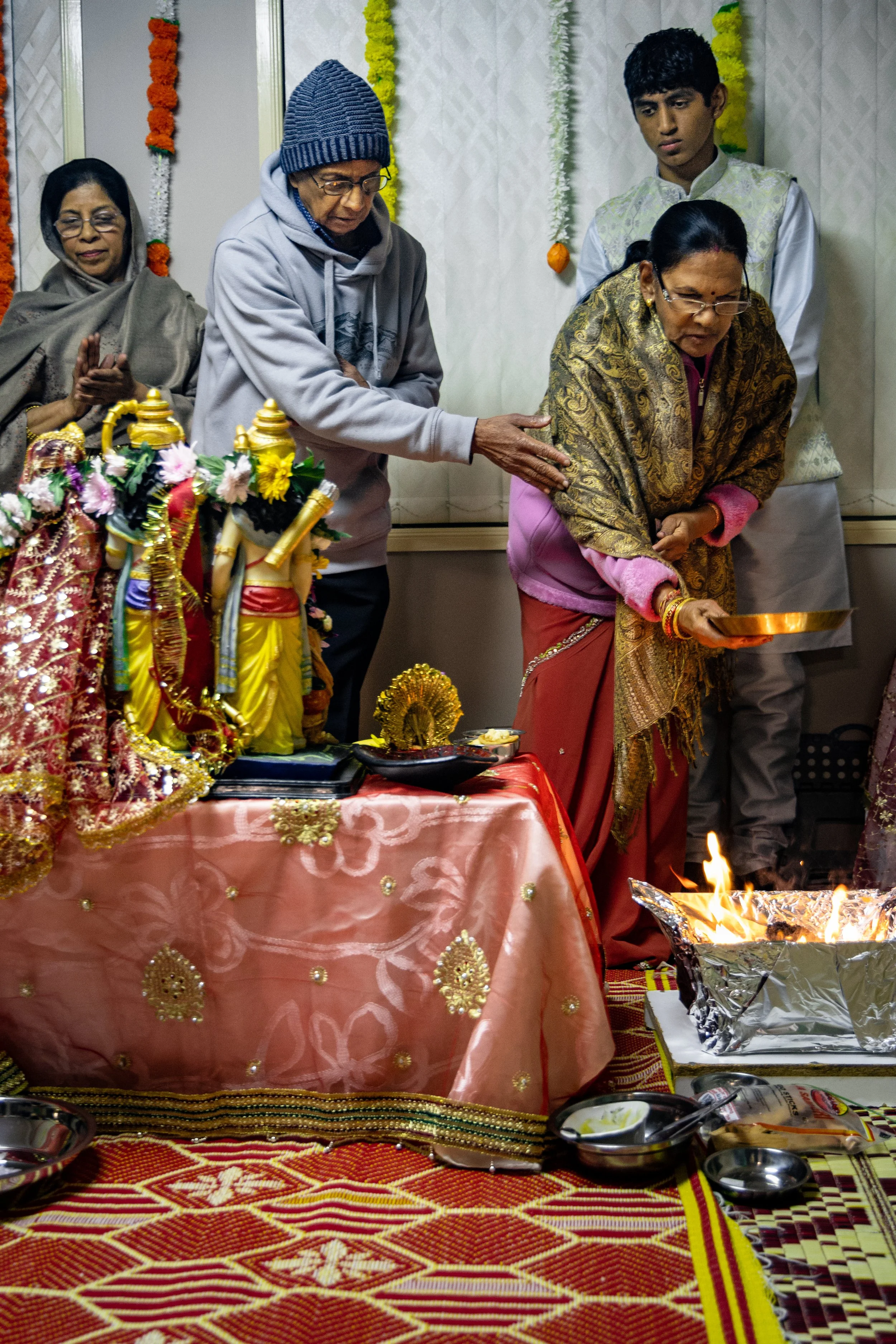 People participating in a traditional Indian religious ceremony, with sacred idols, offerings, and a fire altar.