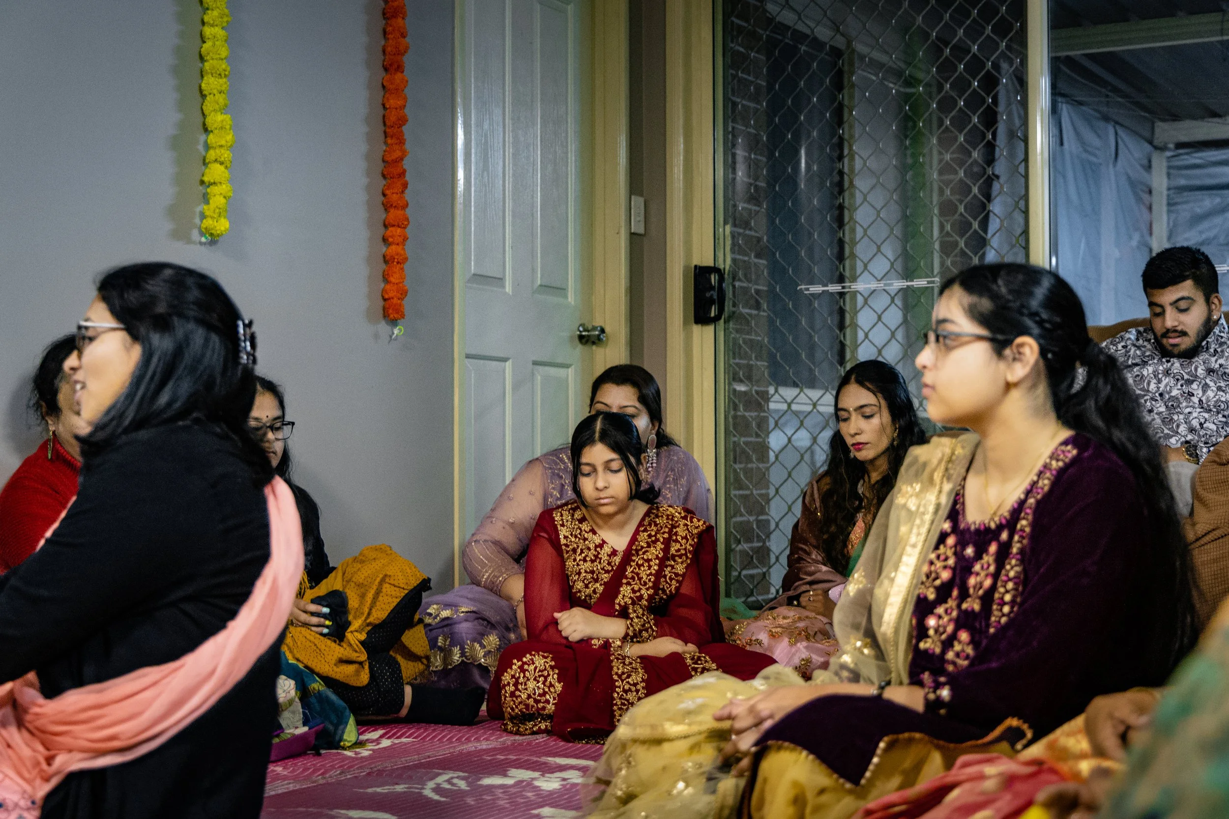 Group of people sitting on the floor in traditional attire during a cultural or religious gathering.