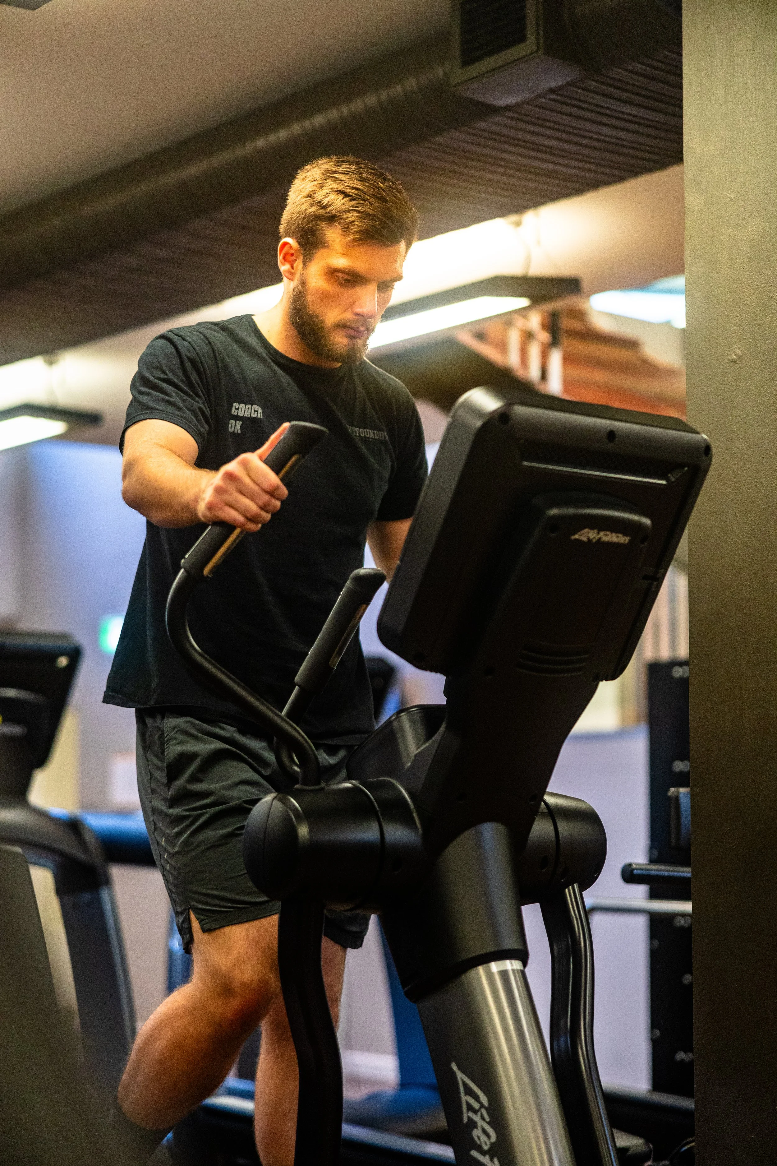 A man with a beard and short hair running on a treadmill in a gym.