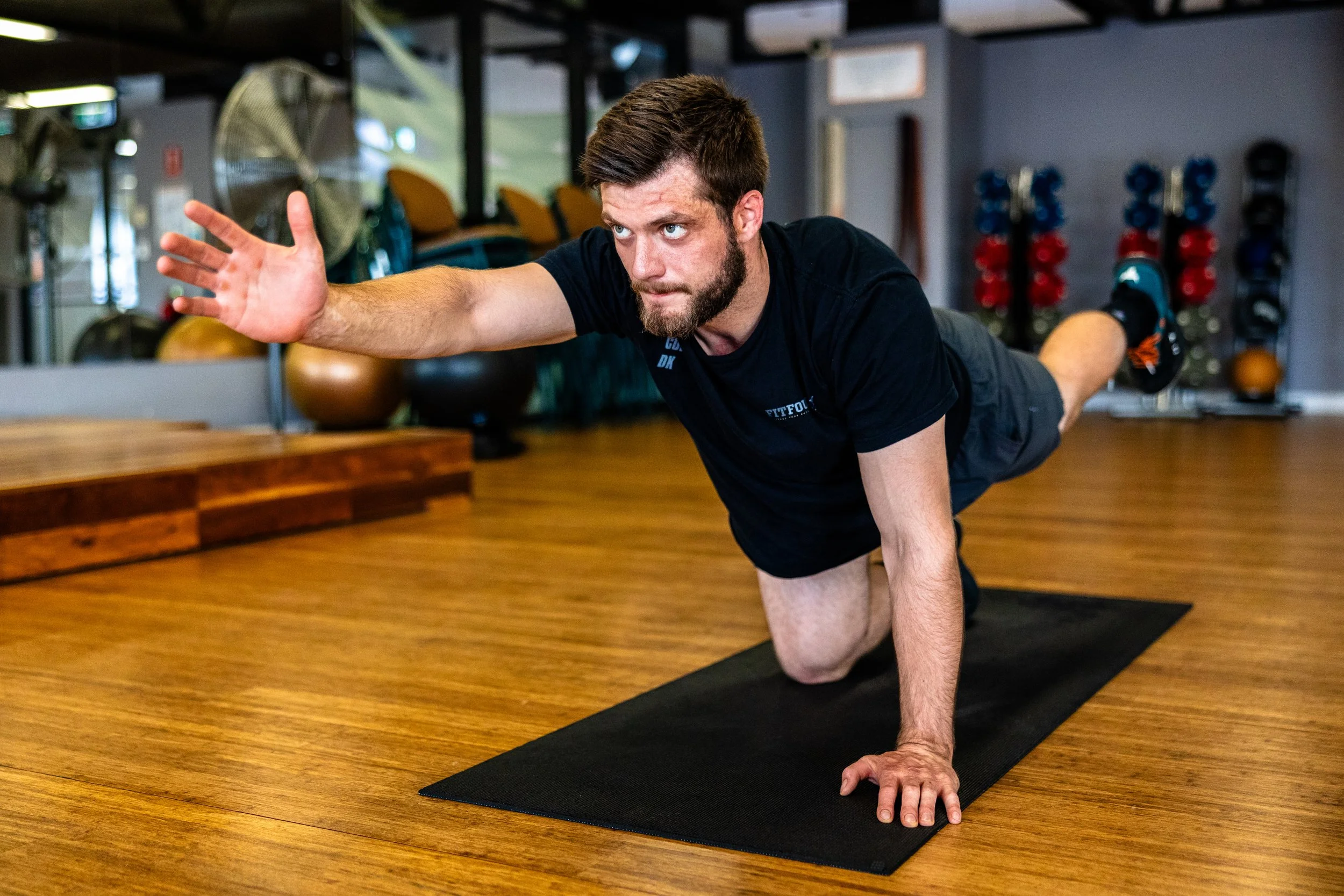 Man performing a stretch on a yoga mat in a gym.