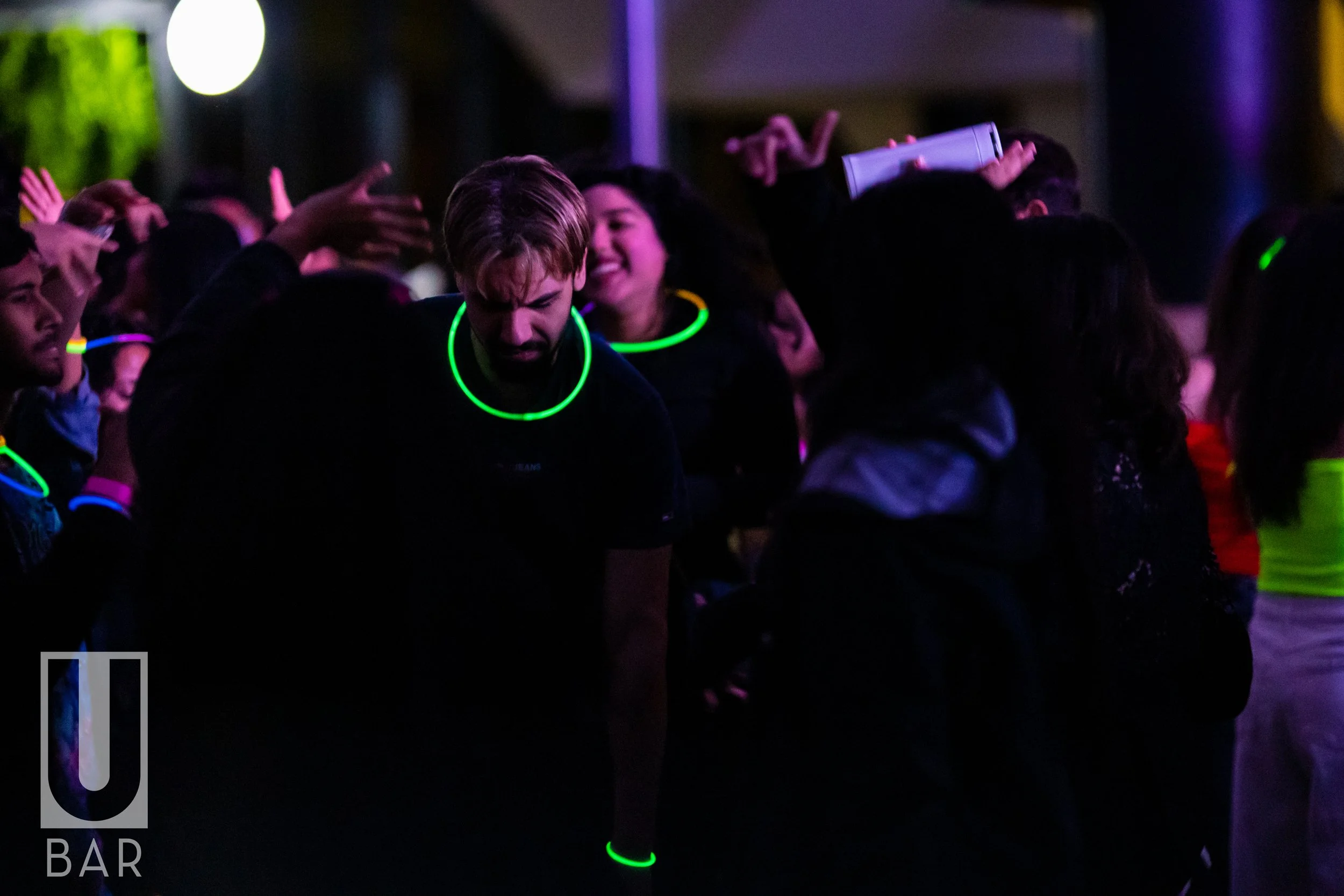People dancing at a party wearing glow necklaces and bracelets in a dark environment.
