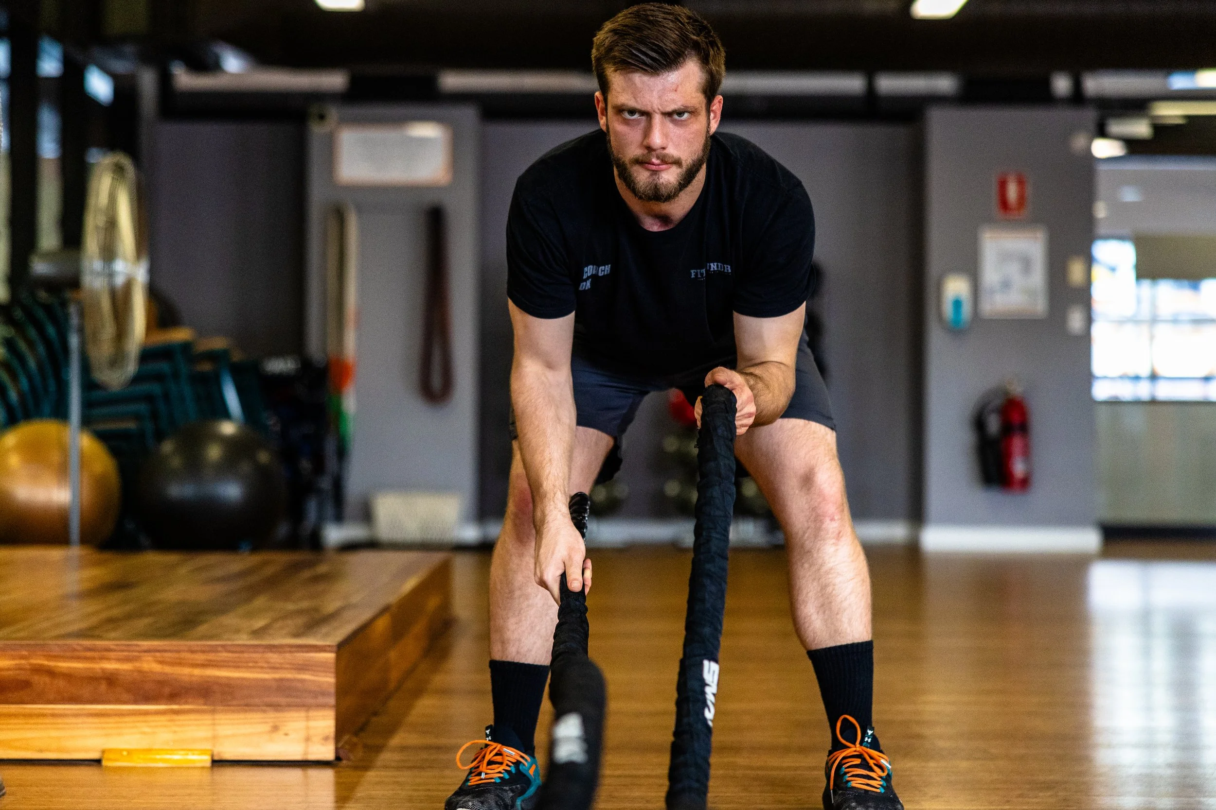 Man with beard and short hair doing battle ropes exercise in a gym.