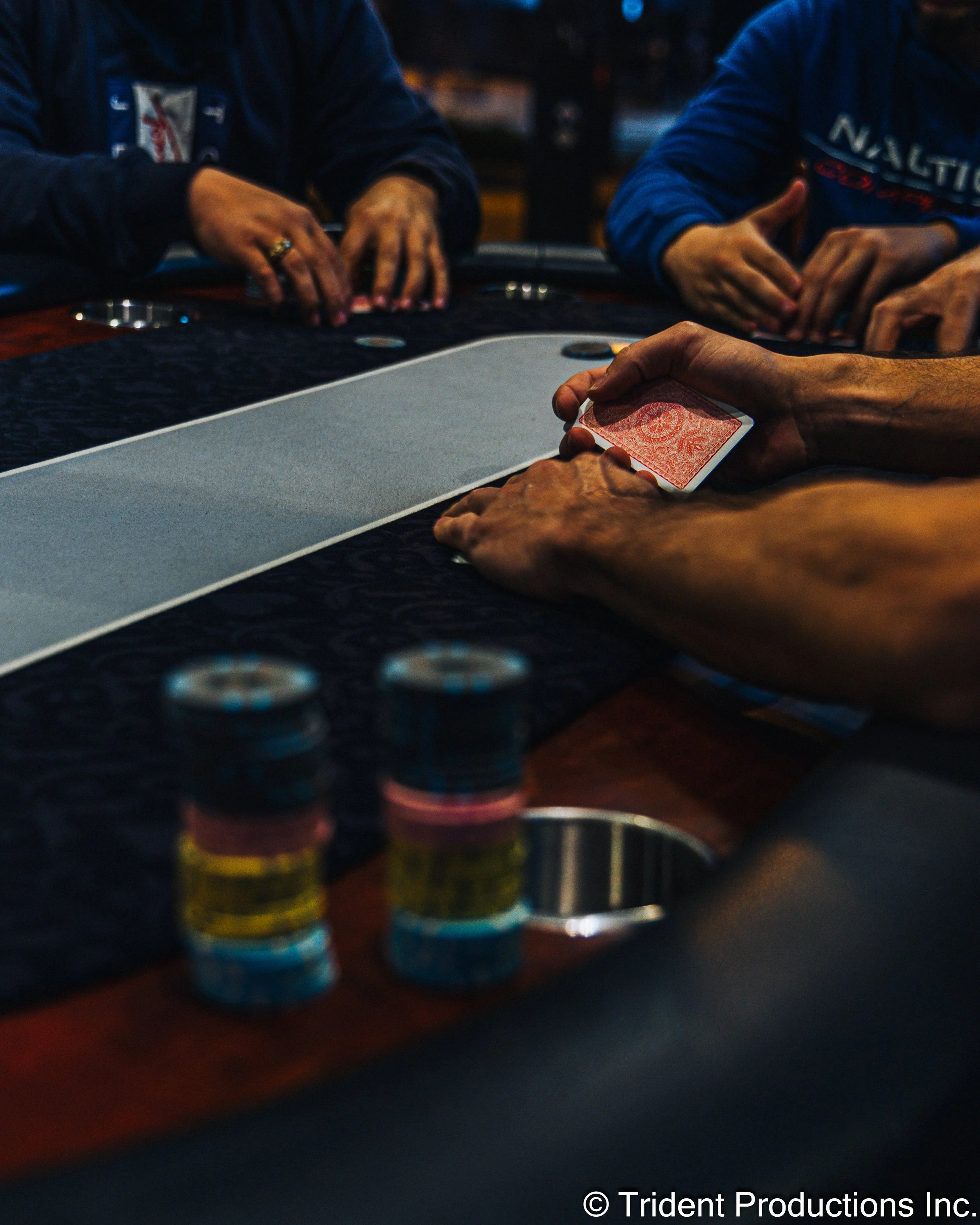 People sitting around a poker table, with one person holding a card, and poker chips stacked in the foreground.